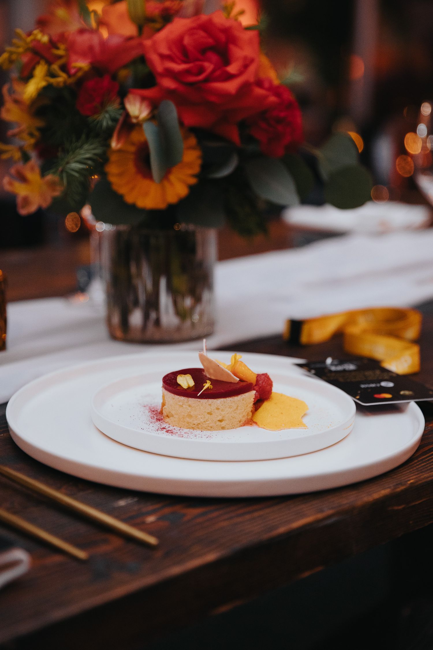 Artistic plating of gourmet dishes with colorful floral arrangements in soft lighting.