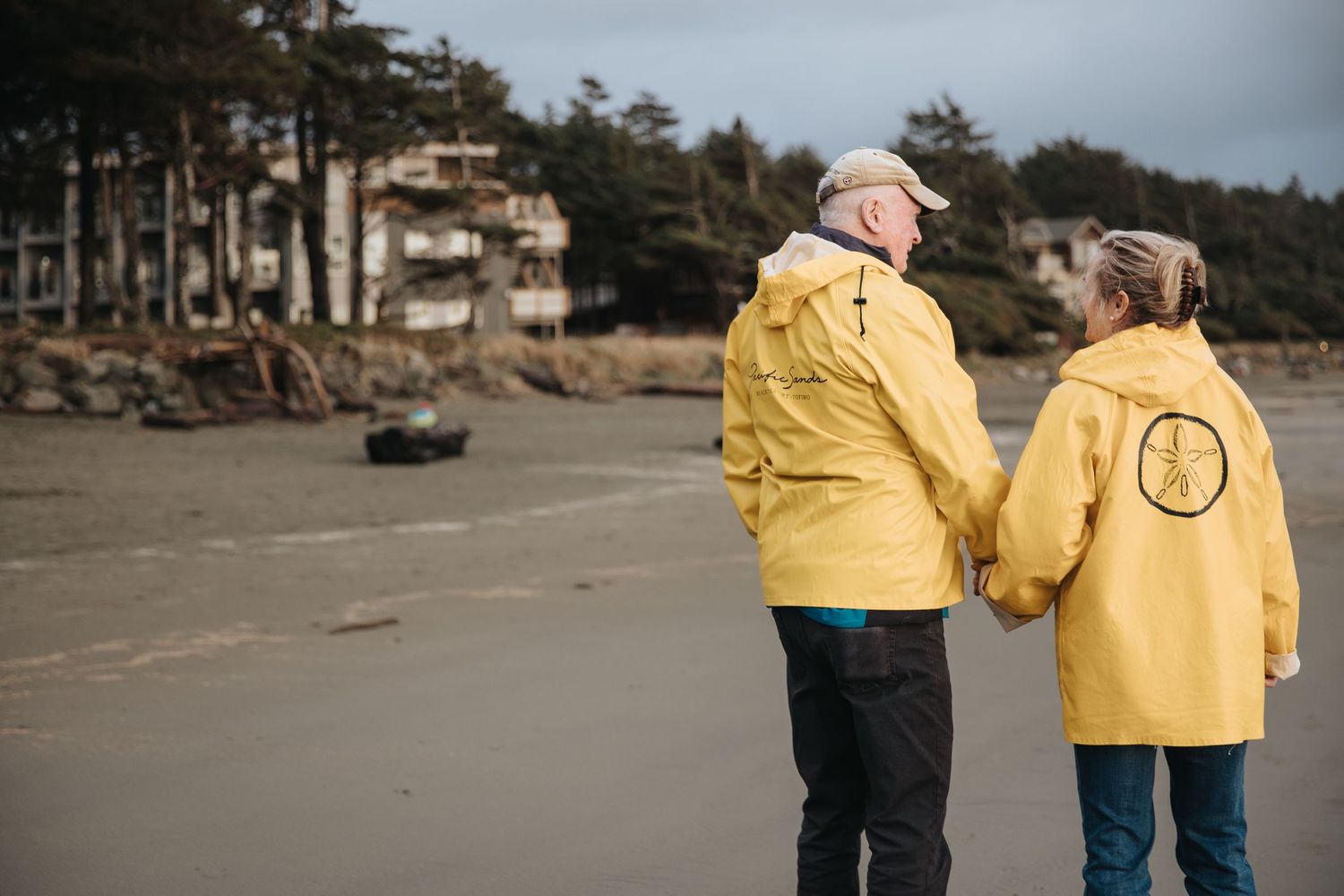 Couple in yellow raincoats walking together on misty Pacific Northwest beach.