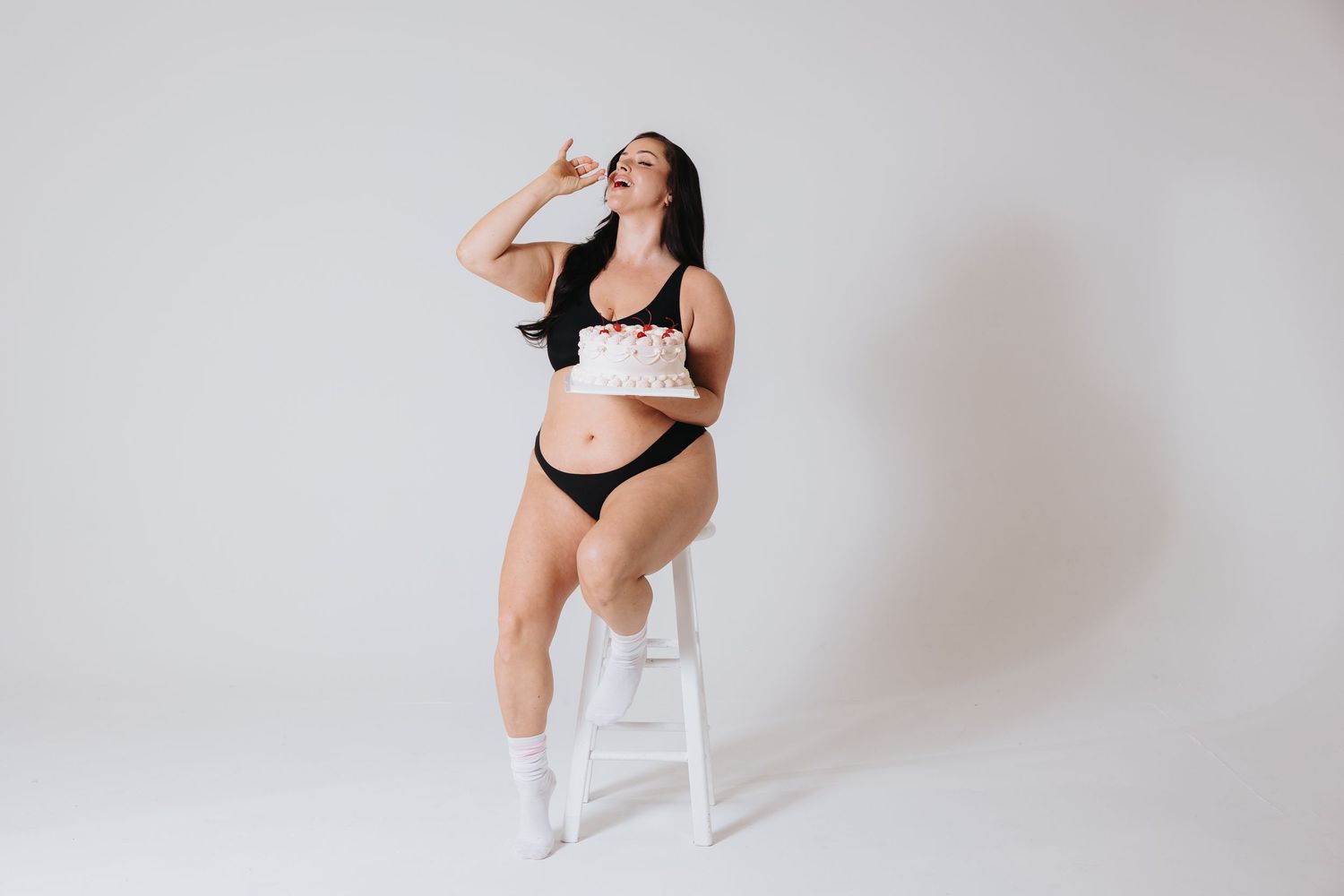 Athletic figure in black workout attire poses gracefully against a white studio background.