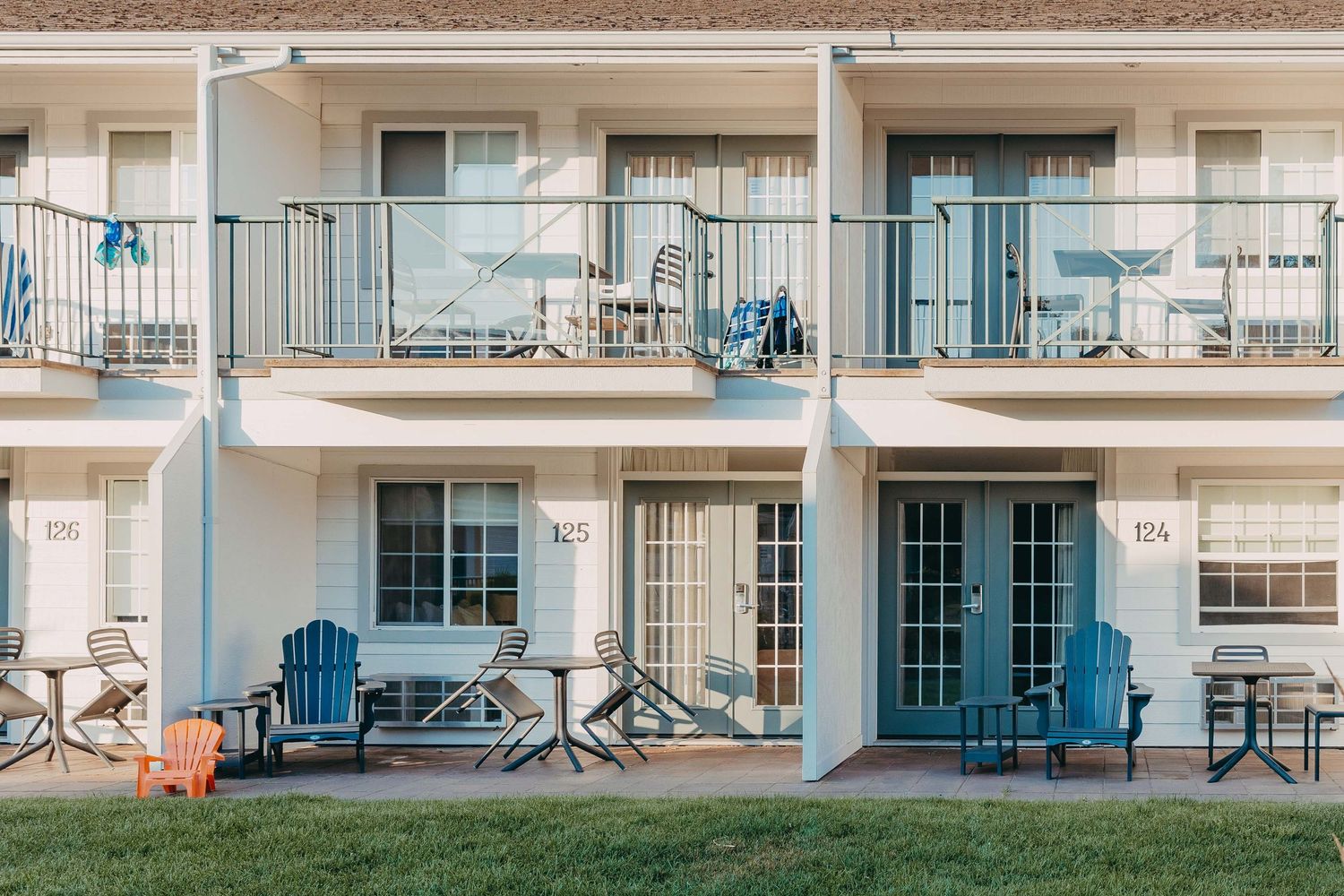 Exterior view of a white apartment complex with blue patio furniture and picnic tables.