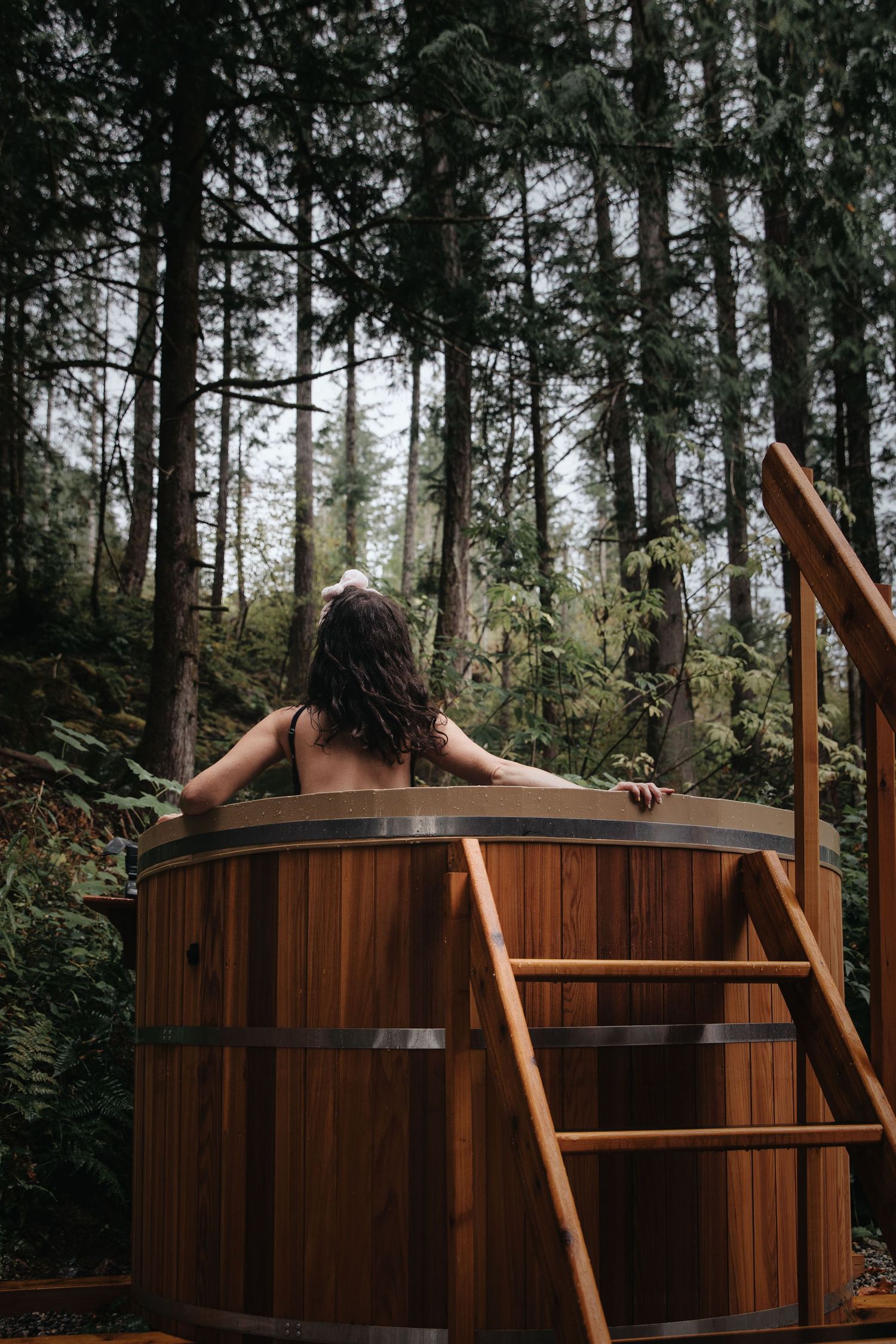 Cedar hot tub nestled among evergreen trees in peaceful forest setting.