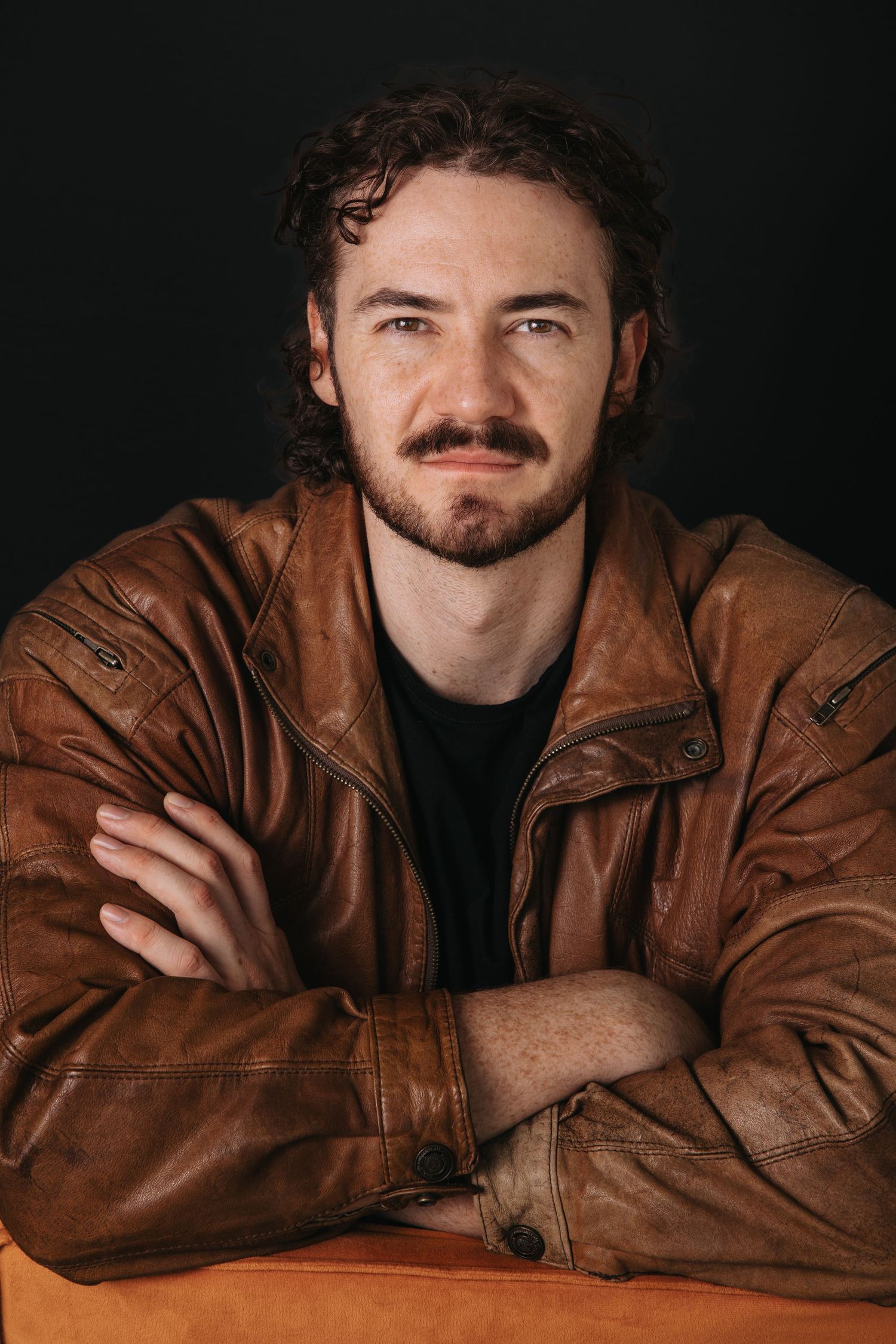 Artistic portrait series in brown leather jacket against dark background.