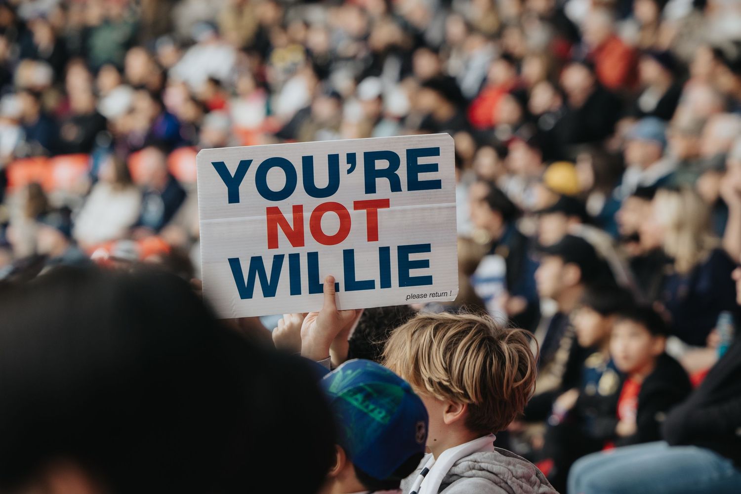 Fans hold up signs in the crowded stadium stands during a sporting event.