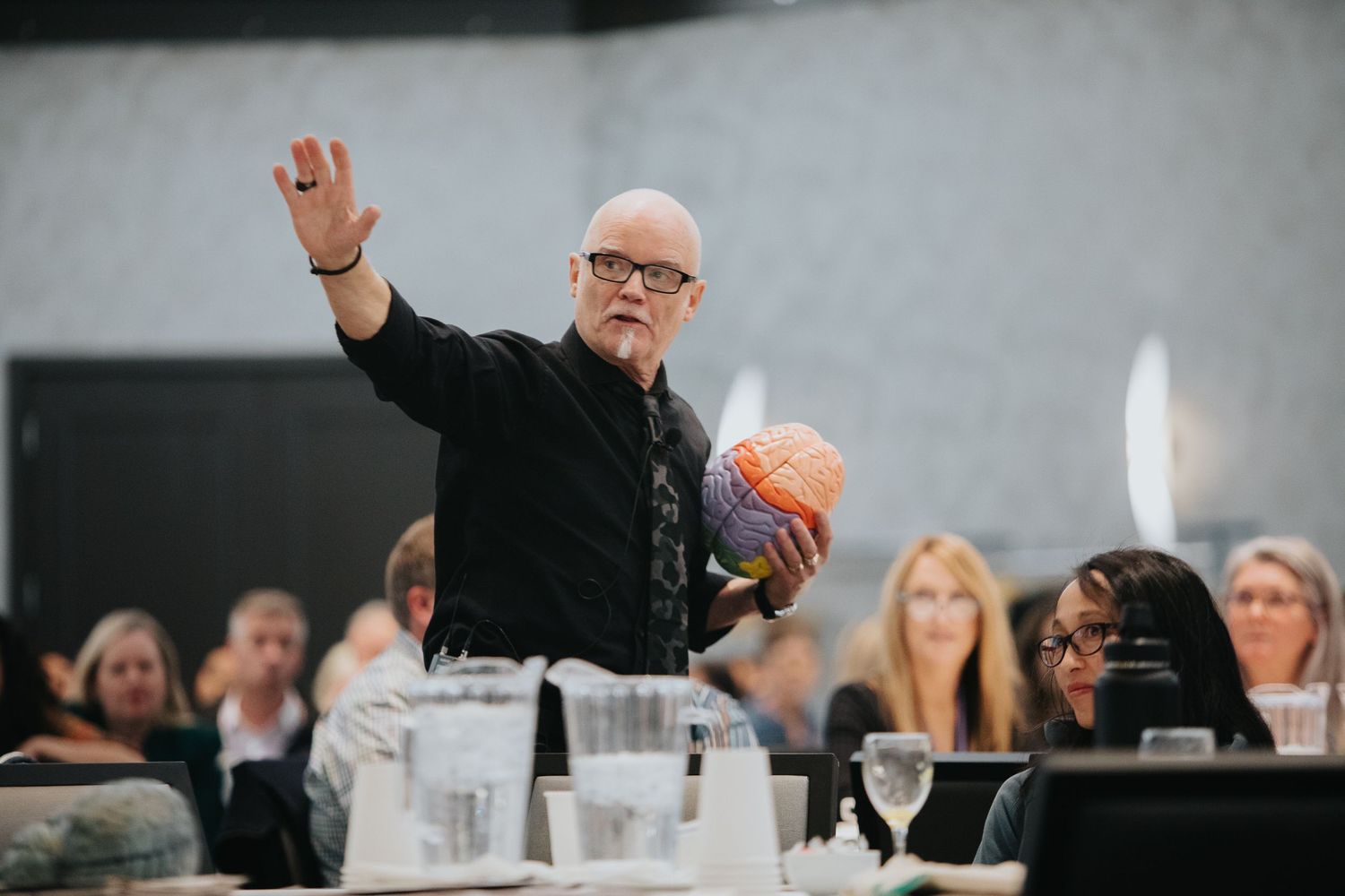 People raising hands and engaging during dinner event at long table.