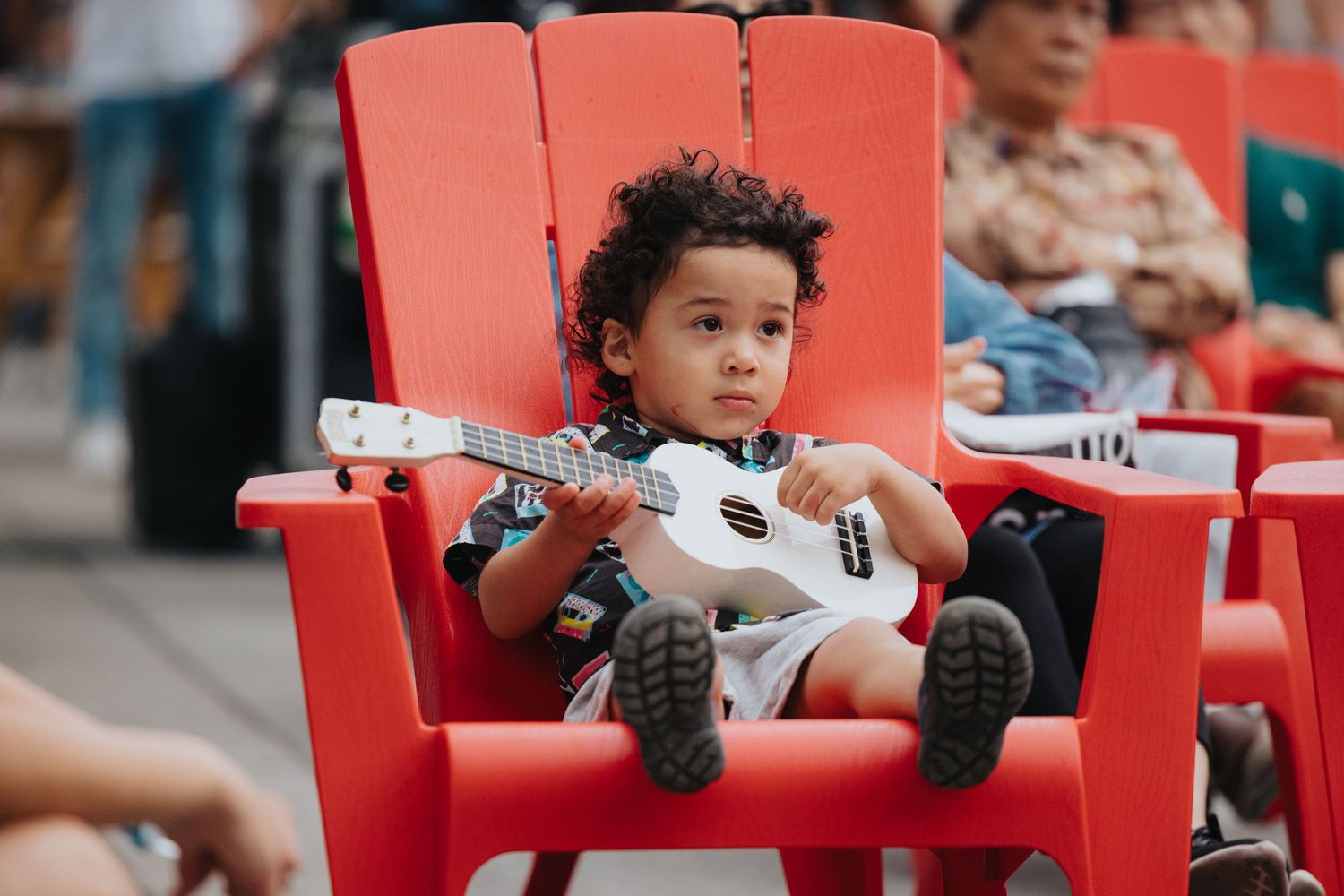 Child sitting in a bright red outdoor chair at a community event.