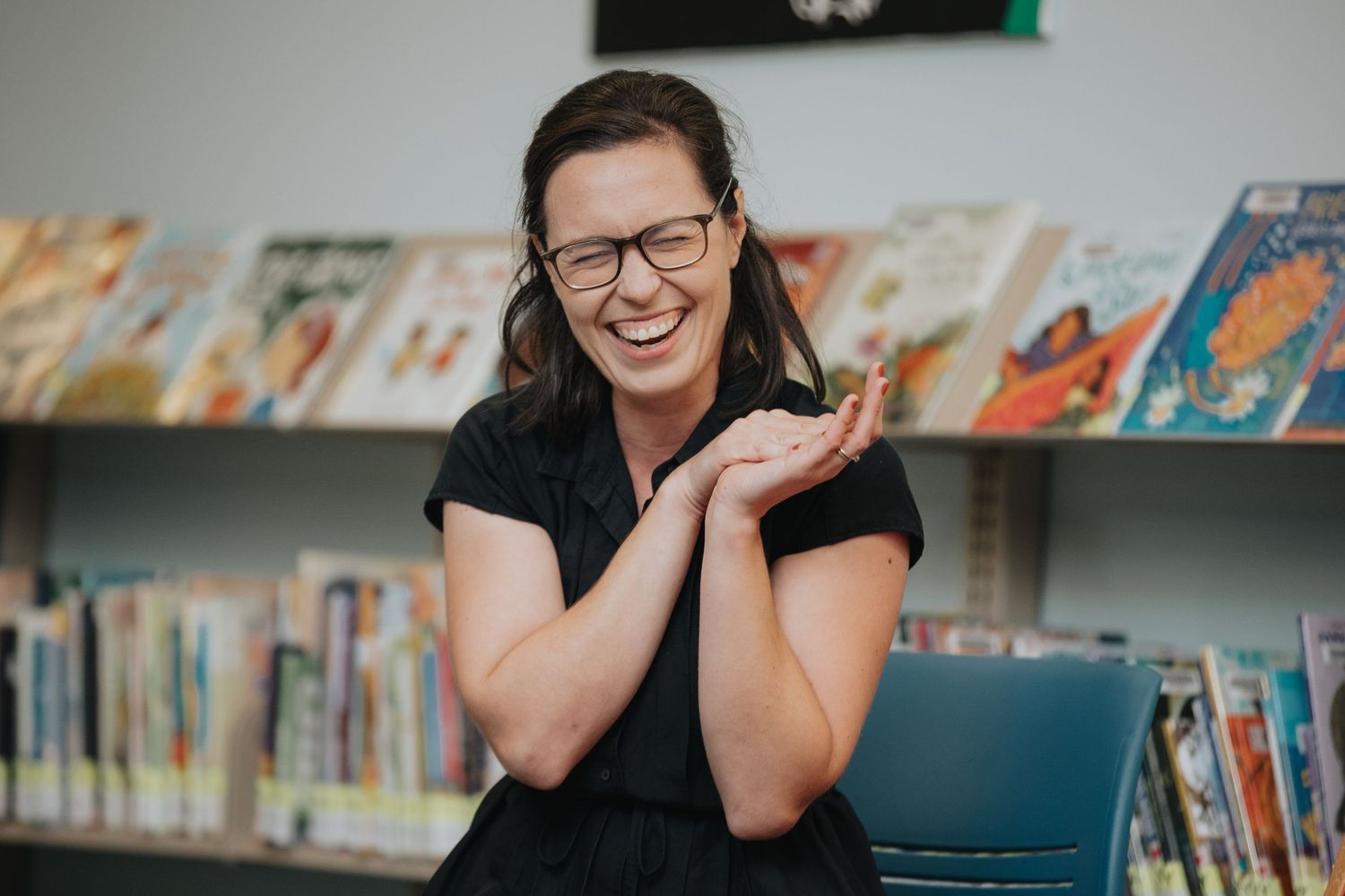 Library staff member wearing glasses smiles while standing near bookshelves.