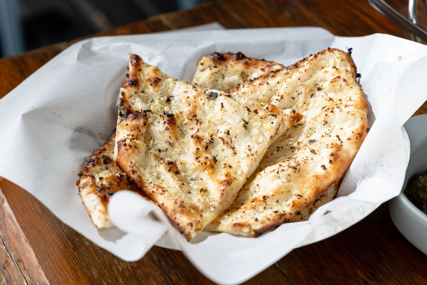 Golden garlic flatbread with herbs, served in a white paper-lined basket on a wooden table.