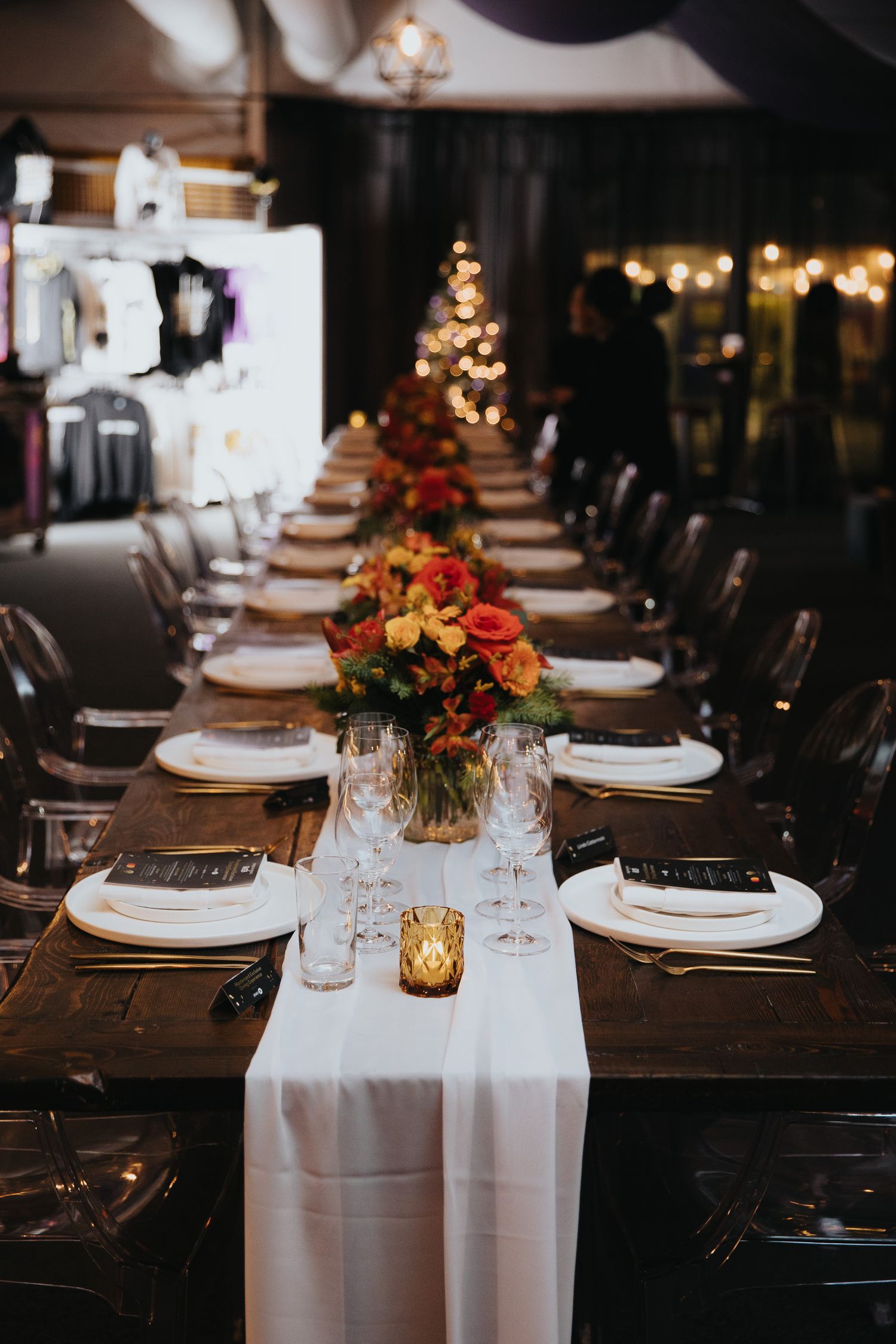 Romantic dinner table setup with candlelight, white linens, and fall-colored flower arrangements.