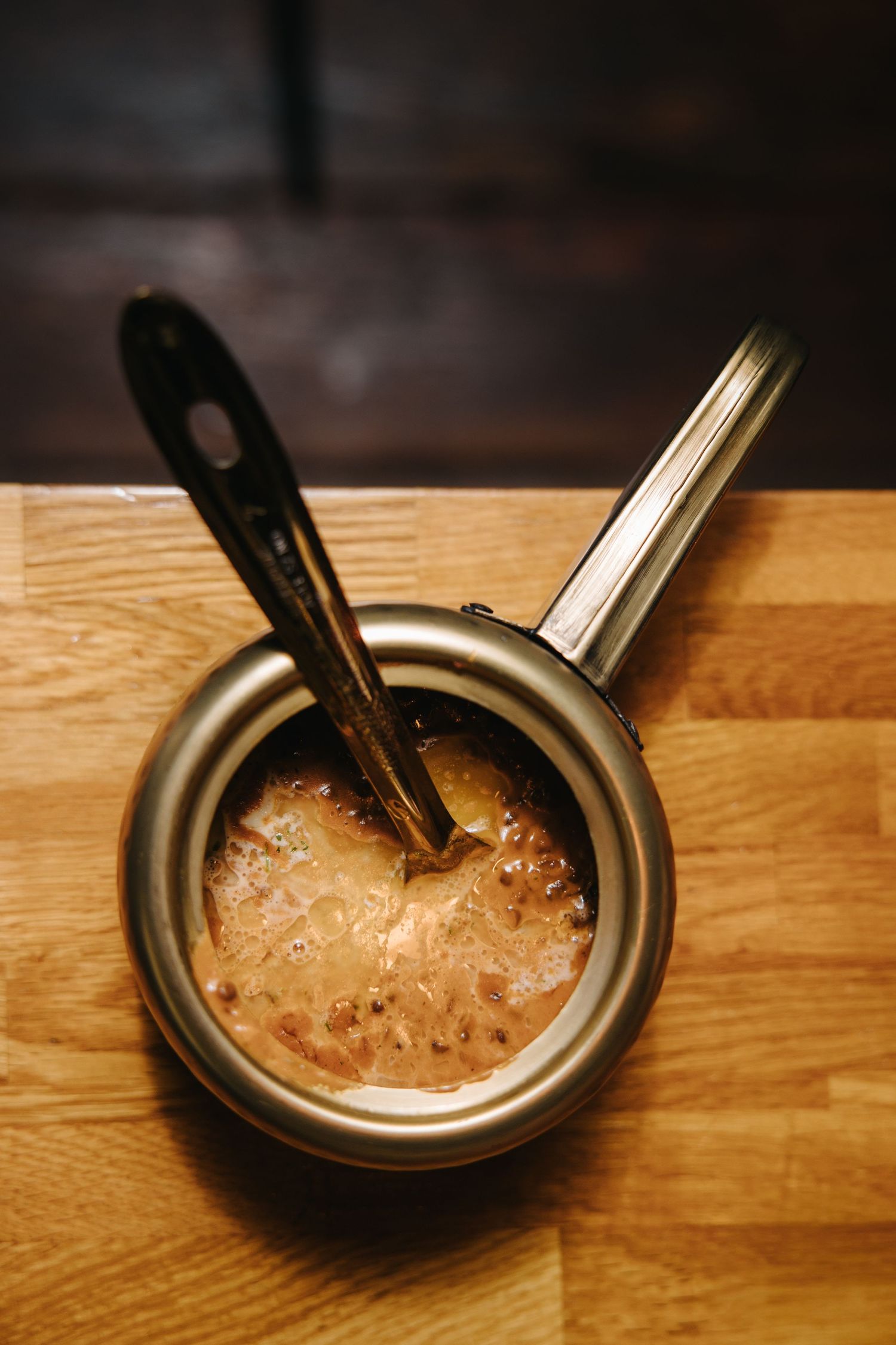 Small saucepan with bubbling caramel sauce and a wooden spoon resting on a wooden cutting board.