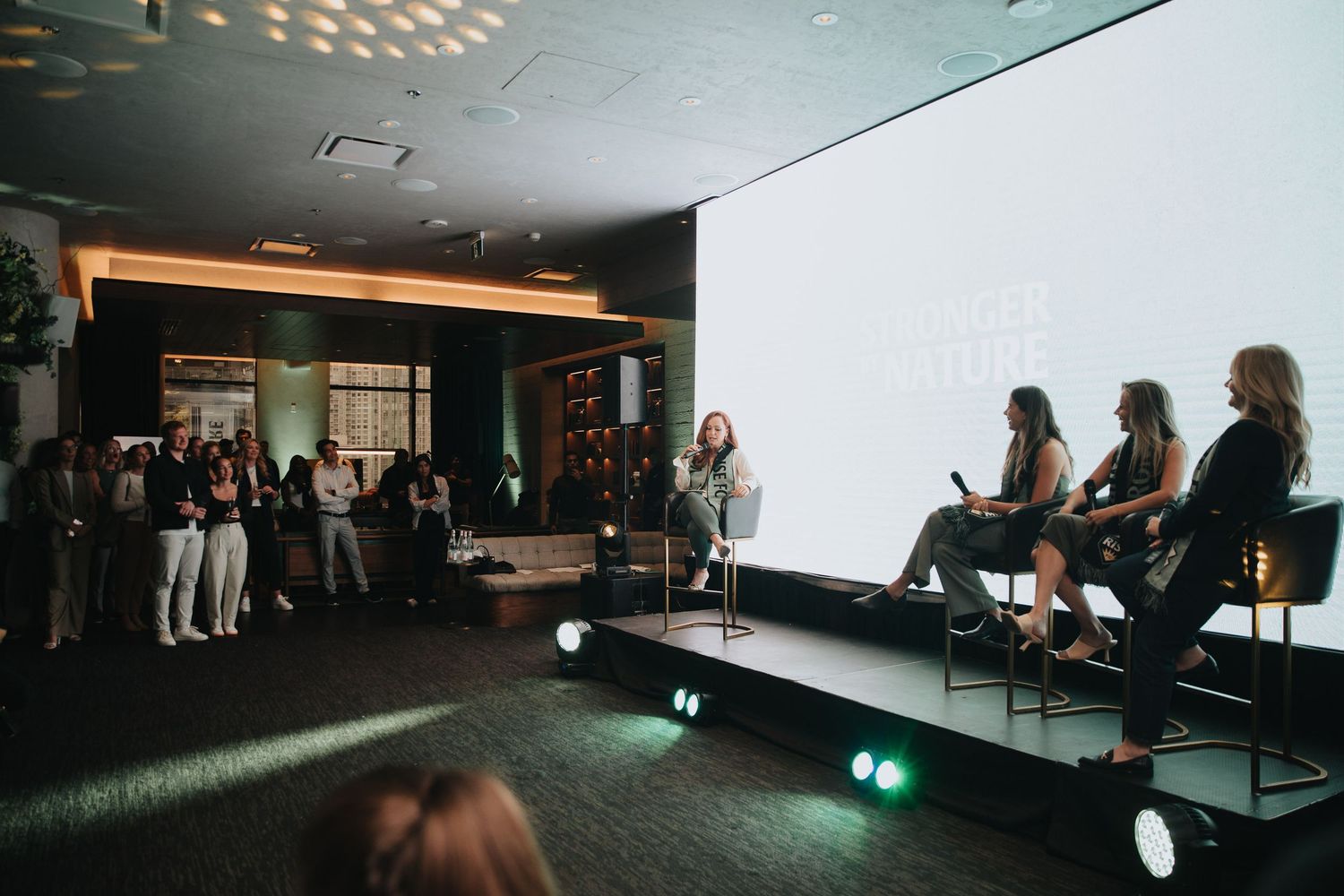 Conference attendees seated in a dark room with spotlights and projection screens during a presentation.