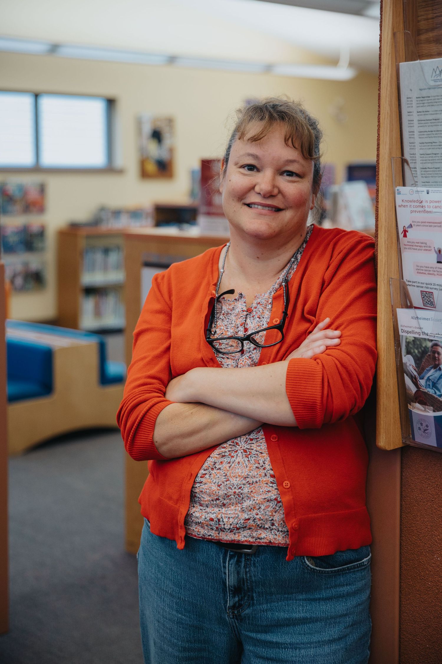 Staff member in orange cardigan poses confidently in library workspace.