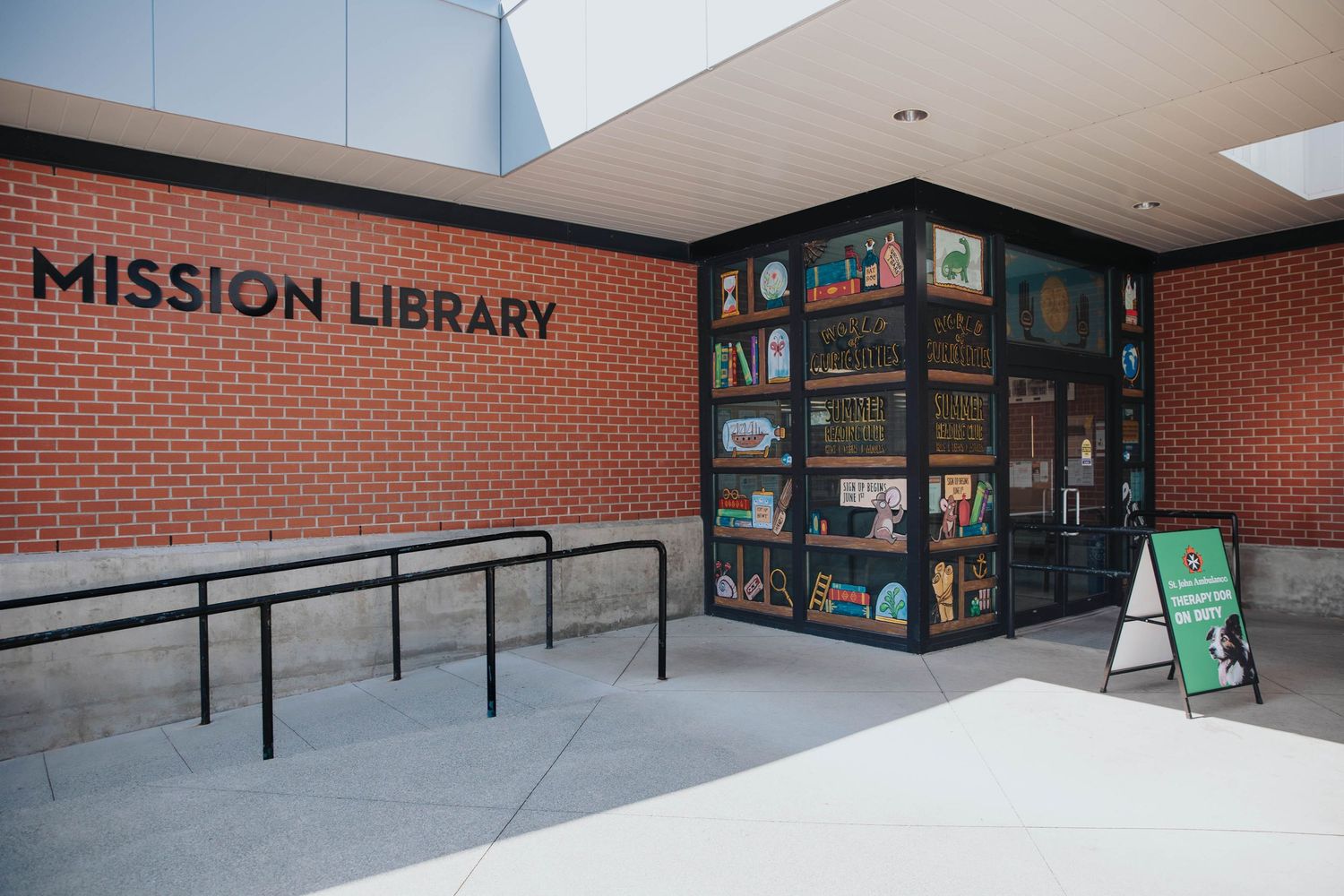 Exterior view of a modern brick library building with entrance ramps and signage.