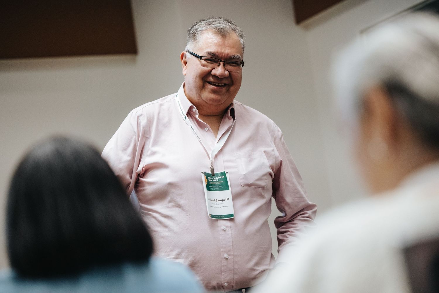 A person in a pink shirt gestures while speaking during what appears to be a business meeting or presentation.