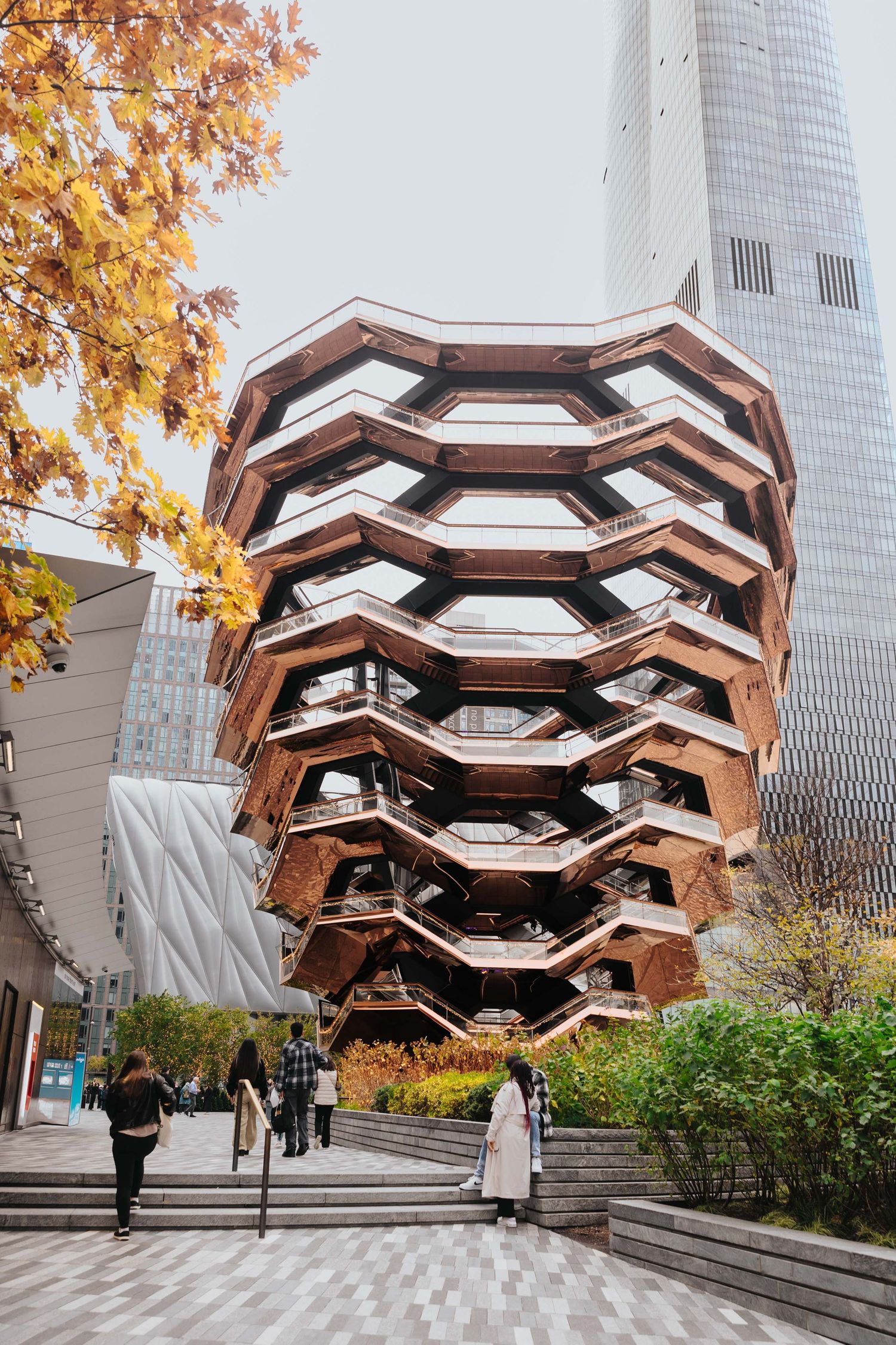 Unique geometric vessel structure with fall foliage and skyscraper in background.