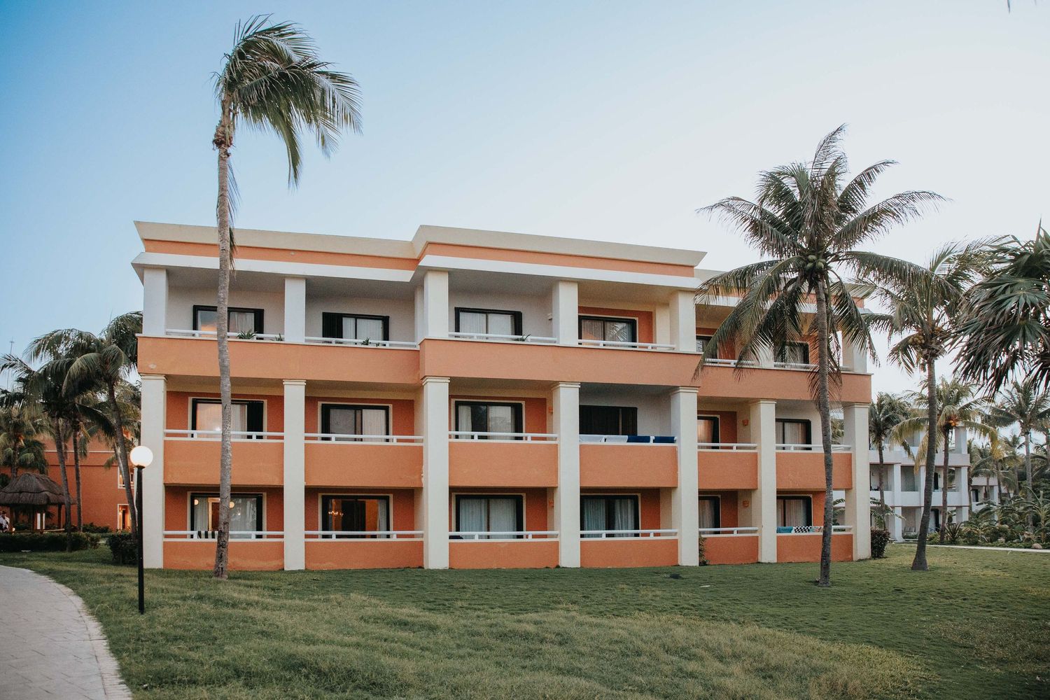 Orange stucco resort buildings with balconies surrounded by tropical landscaping.