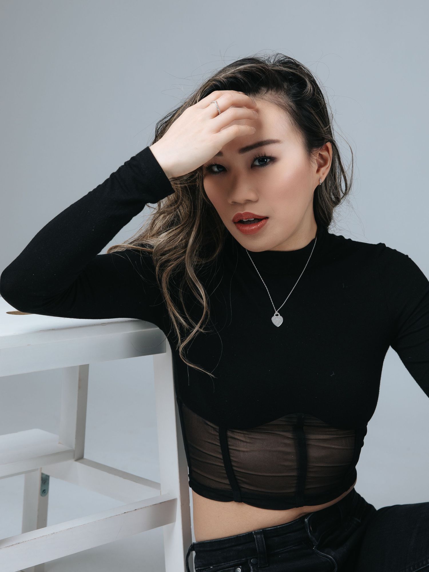 Fashion model in black crop top poses against white wall in artistic portrait series.