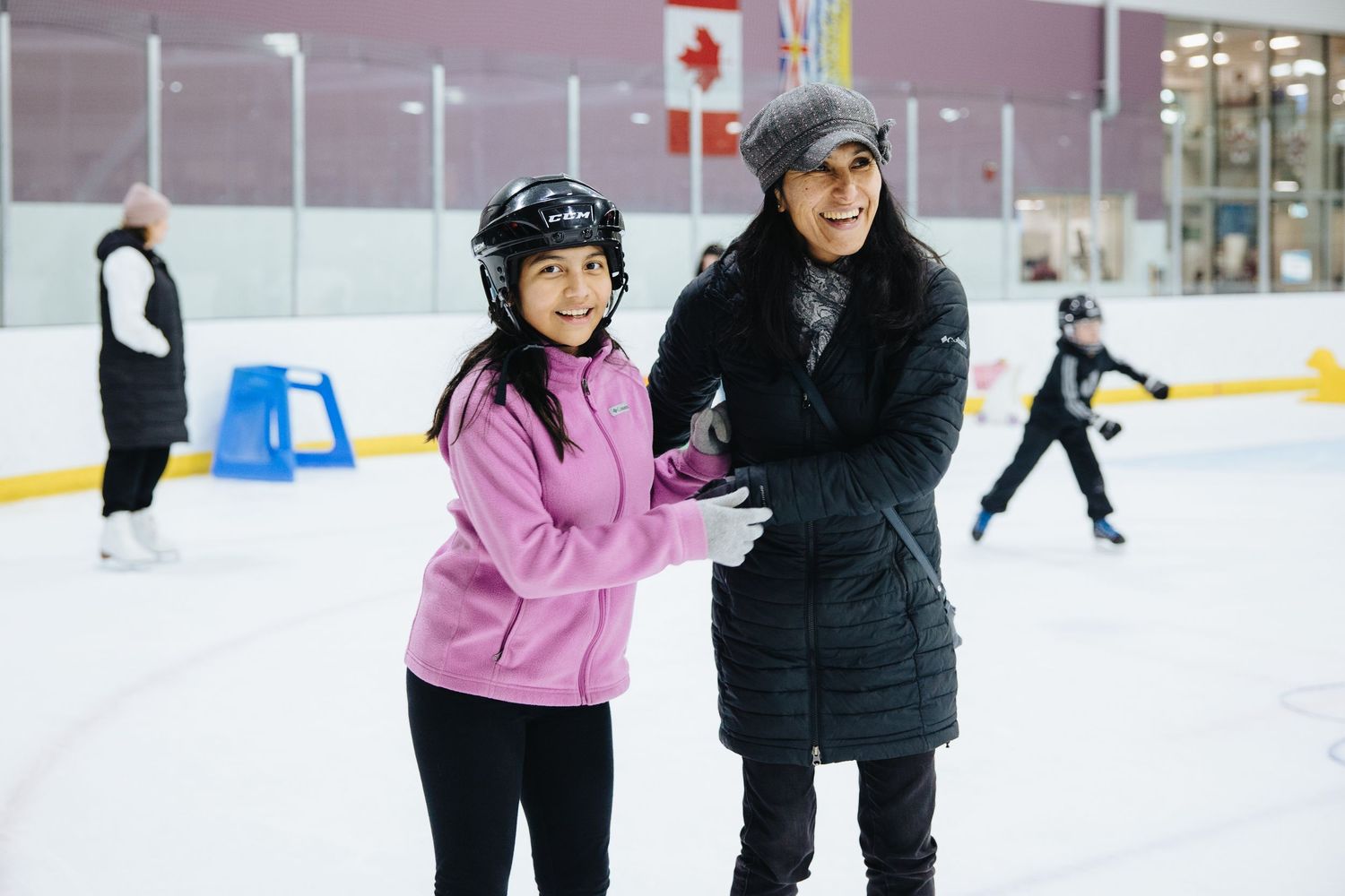Ice skating students learn basic techniques with instructors on a rink.
