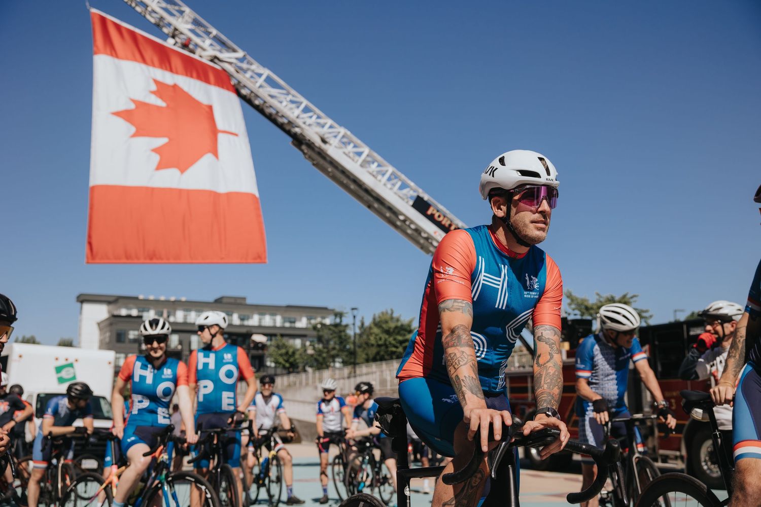 Cyclists and spectators gathered under Canadian flags at an outdoor event.
