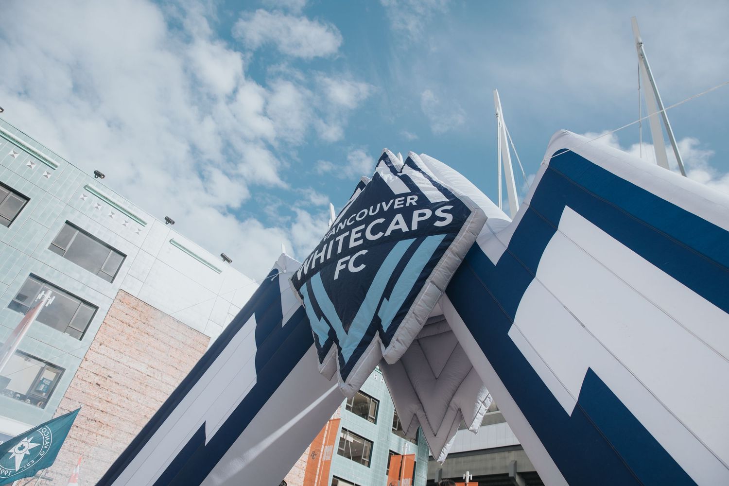 Whitecaps FC logo and signage on modern stadium exterior against blue sky.