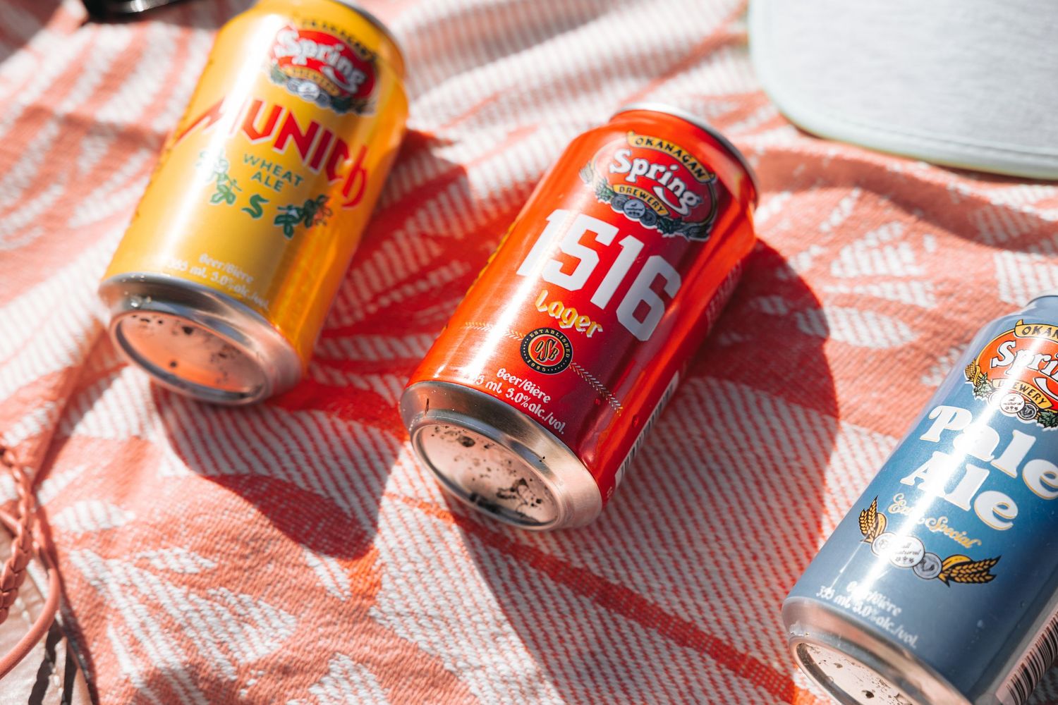 Spring Valley soda cans arranged on a pink and white checkered surface in sunlight.
