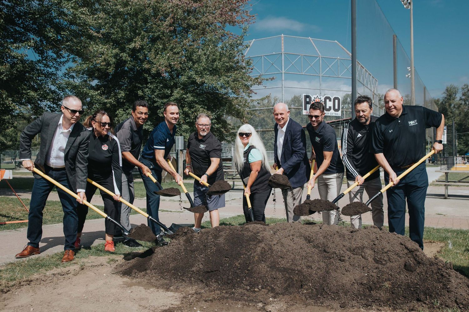 Group of people participating in a ceremonial groundbreaking event with shovels outdoors.