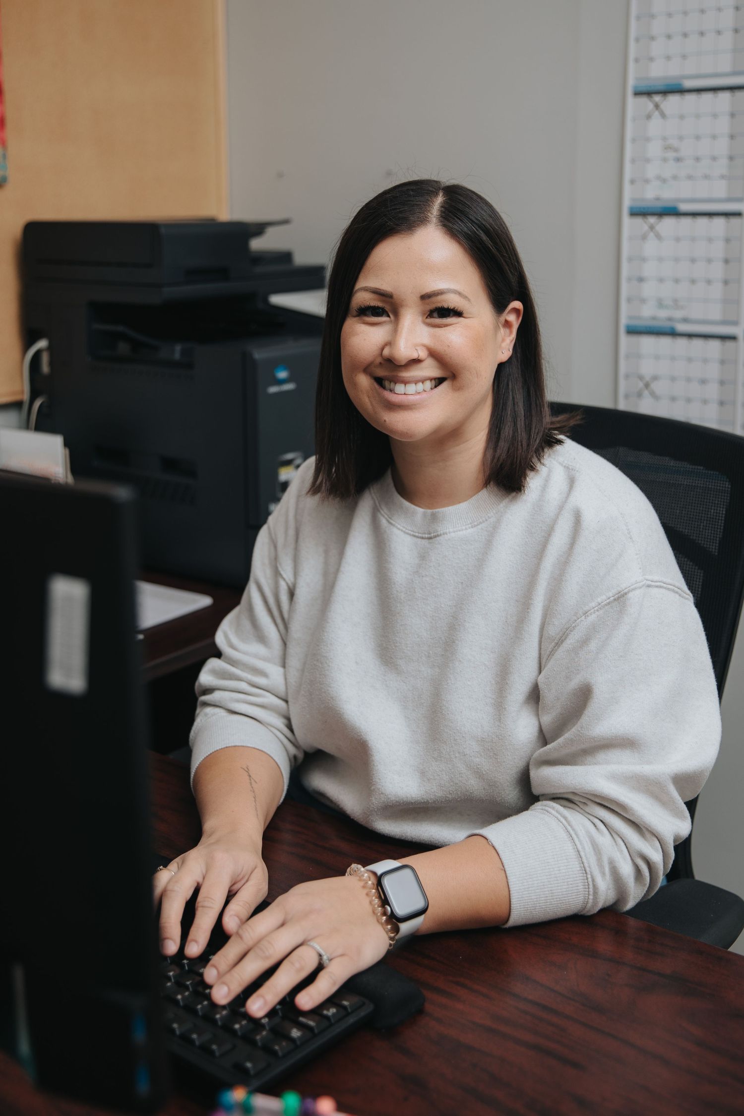 Person in light sweater working at desk with computer mouse.