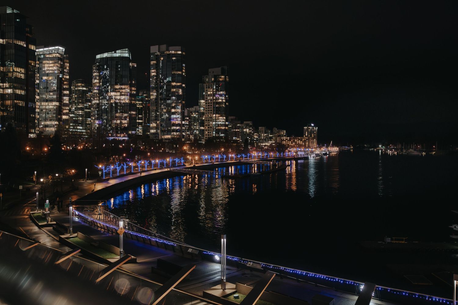 Vancouver cityscape at night reflecting on harbor waters with colorful lights.