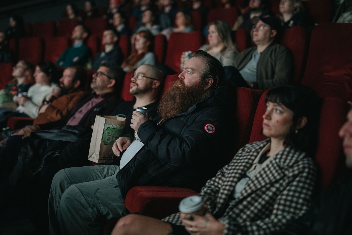 Audience members watching intently in a theater with red seats.