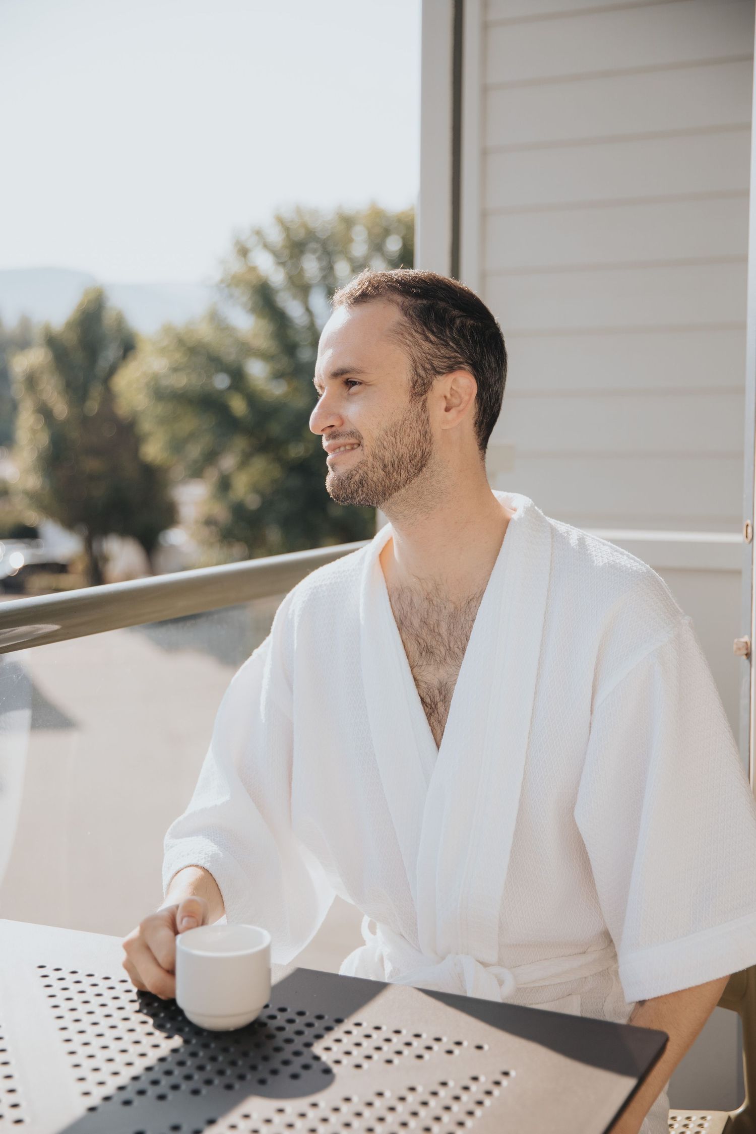 Person in white bathrobe enjoying morning coffee on outdoor patio.