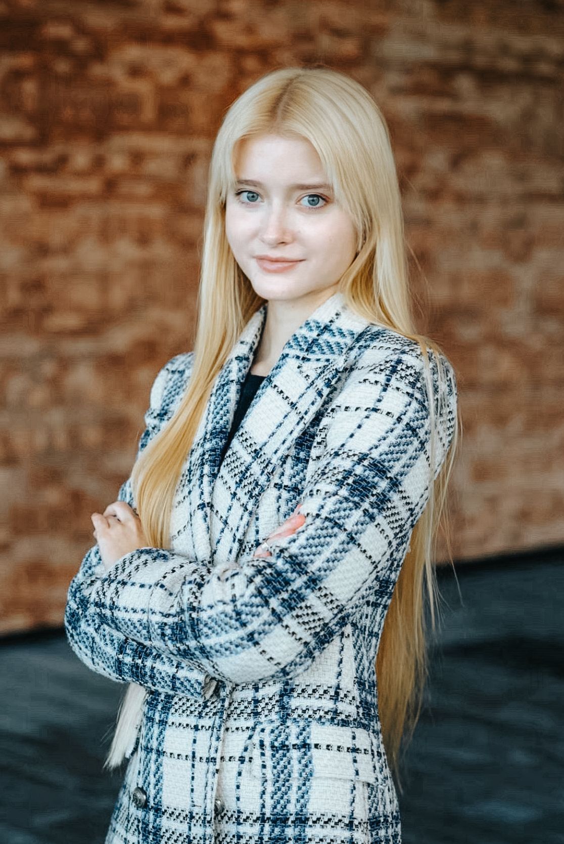 A person wearing a cozy black and white plaid scarf poses against a rustic brick wall background.