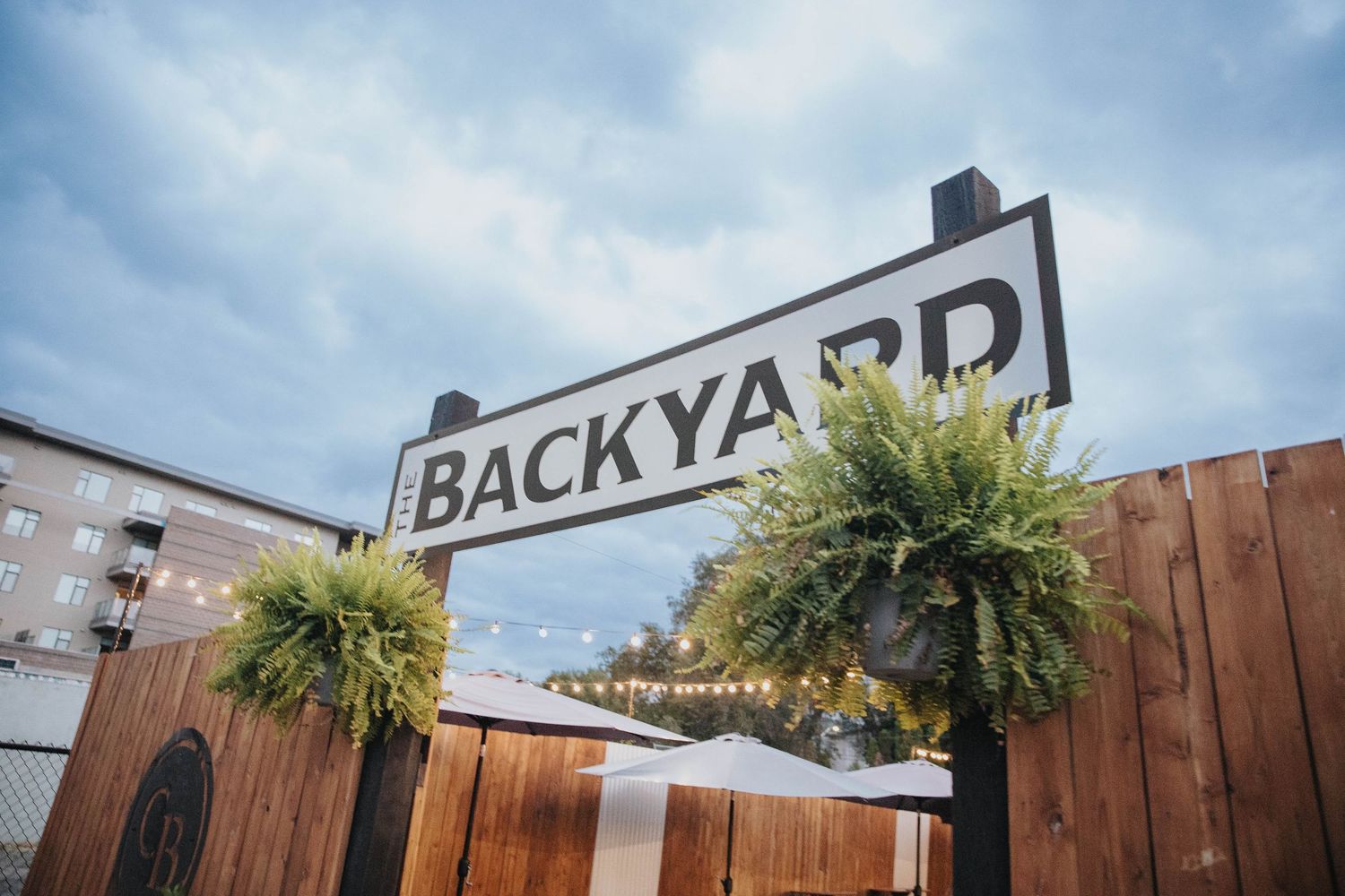 Wooden fence with hanging plants against a blue sky and backyard sign.