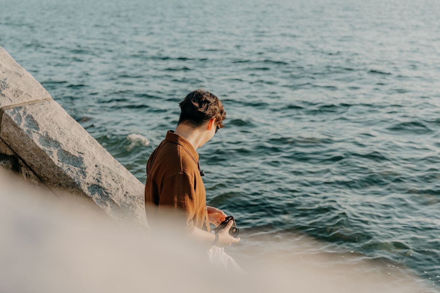 Person walking along a scenic rocky coastline with waves crashing against the shore.
