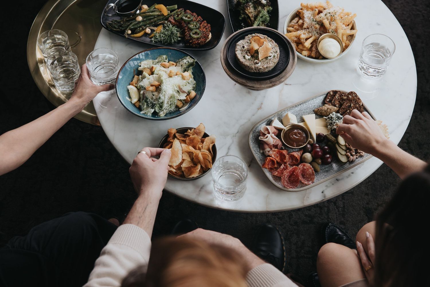 Overhead view of shared plates and appetizers on a restaurant table during a social dining experience.