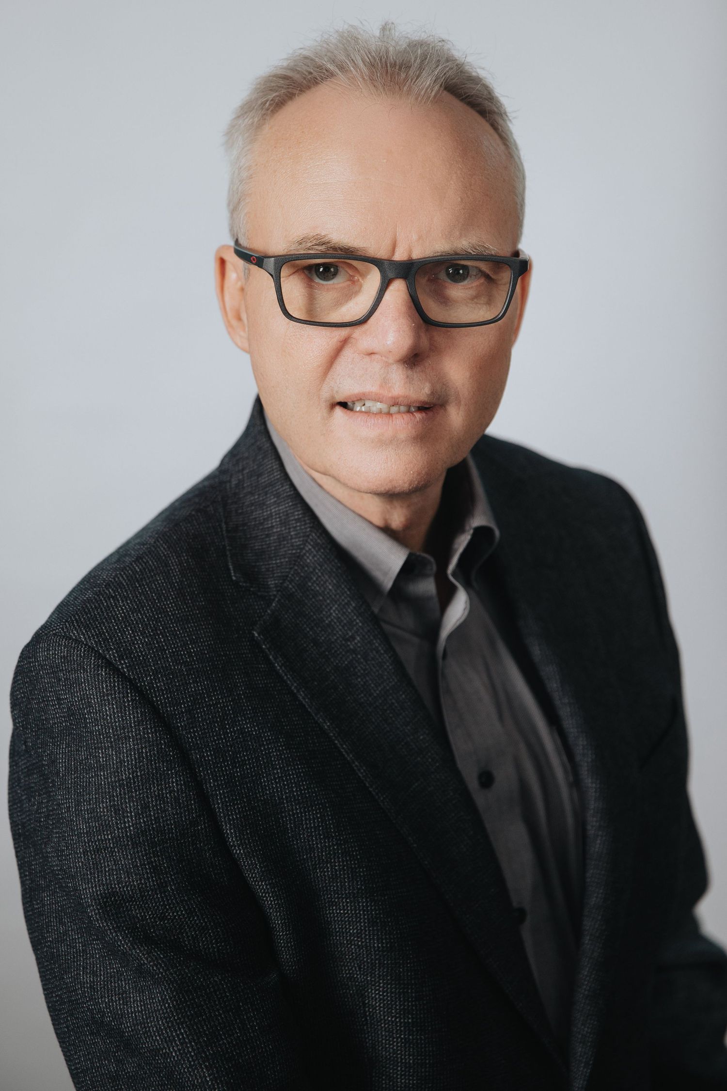 Professional headshot series showing a person in glasses and dark blazer against light background, captured from different angles.