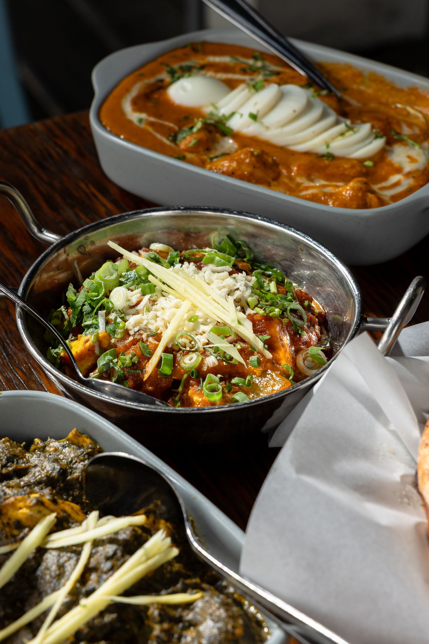 A spread of Indian dishes including curry, a garnished vegetable dish, and spiced greens served in traditional bowls.