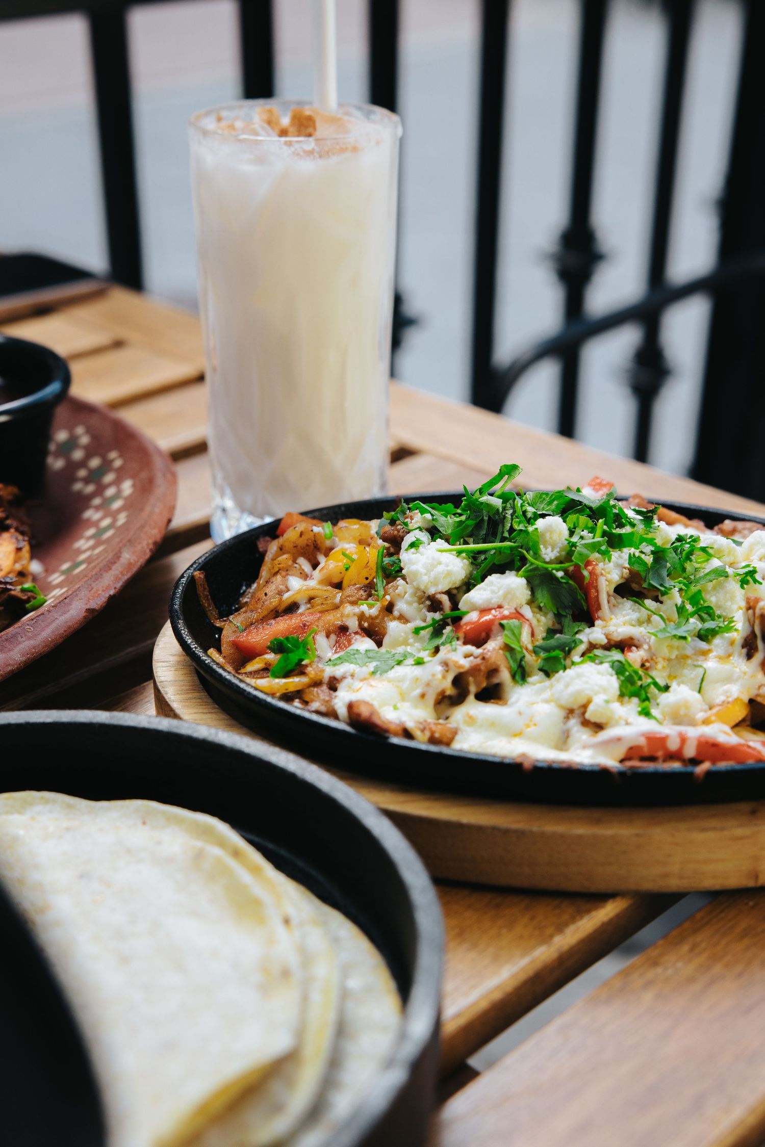 Mexican food dishes and drinks served on wooden tables with iron railings.