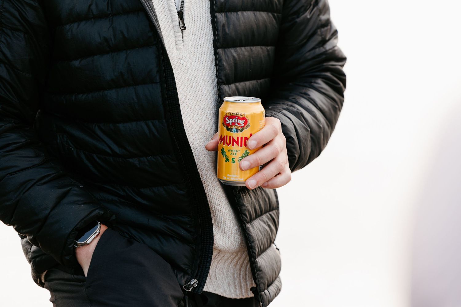 Individual wearing a black puffer jacket poses while holding a drink.