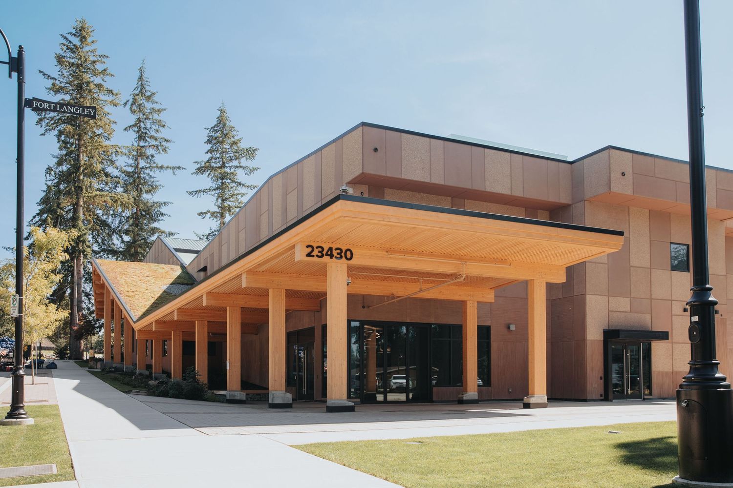 Modern commercial building exterior with wood accents and tall evergreen trees.