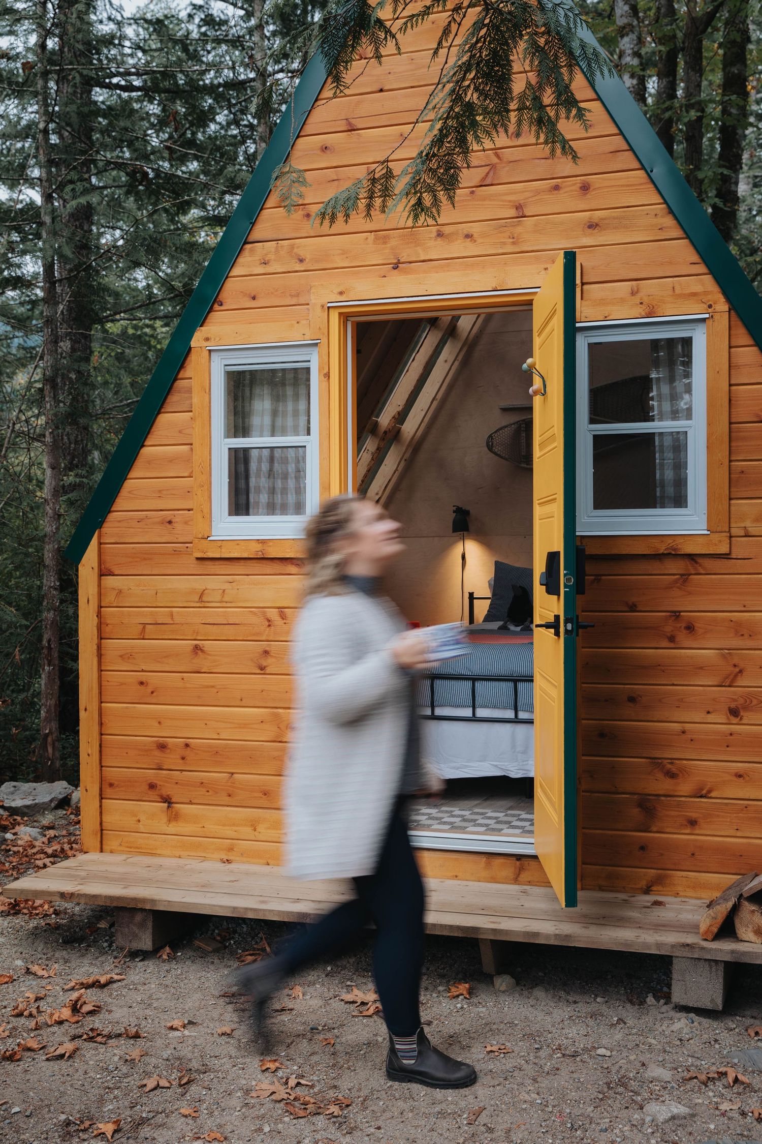 Motion blur of person running past wooden A-frame cabin in forest setting.