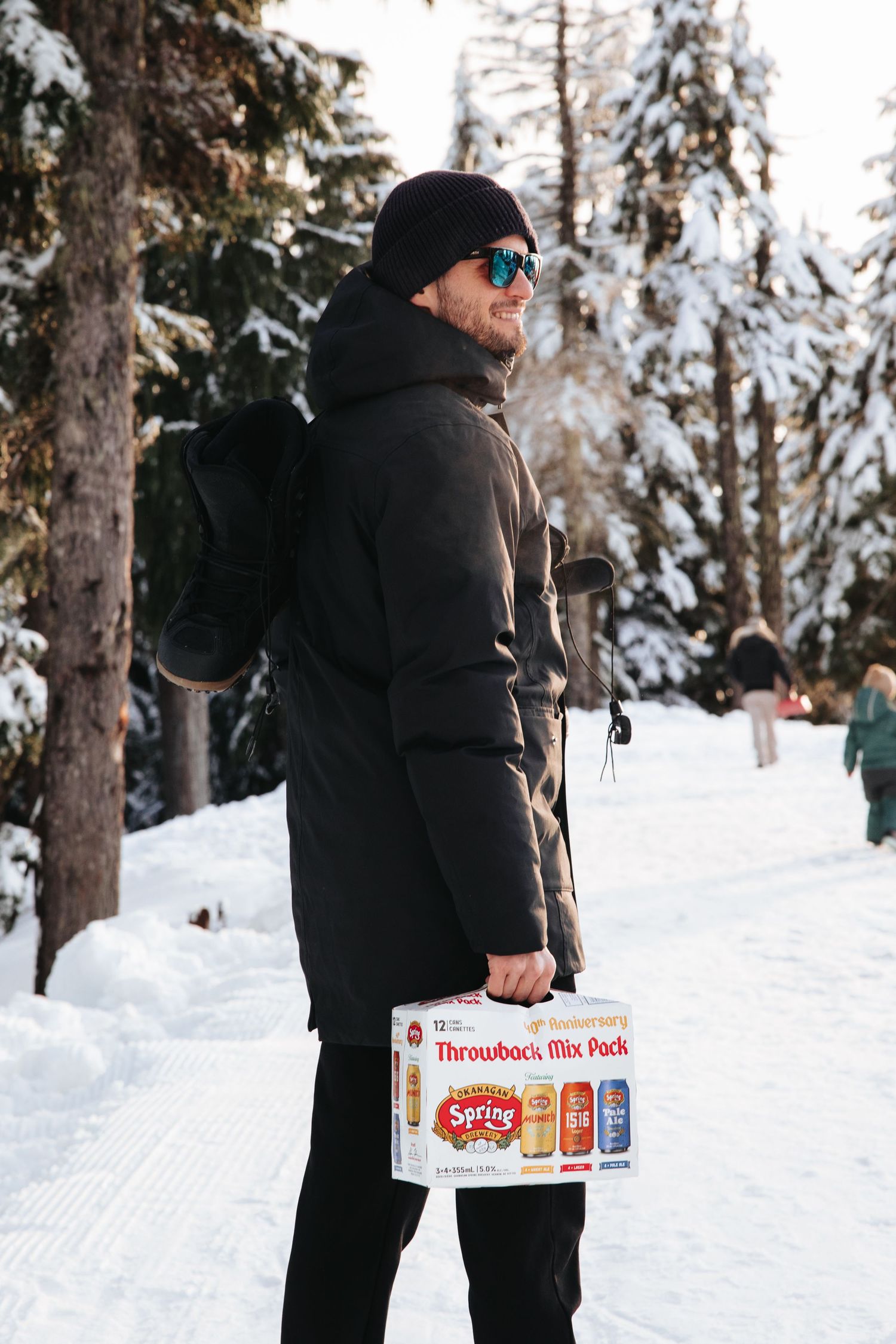 Winter scene with person carrying a case of drinks through snowy forest.