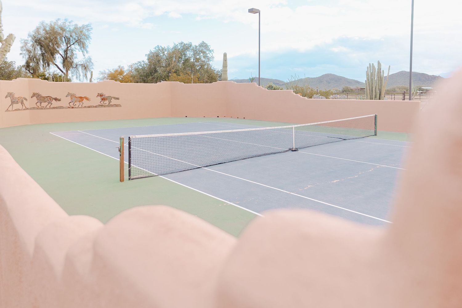 Empty tennis courts with desert mountains in the background under blue sky.