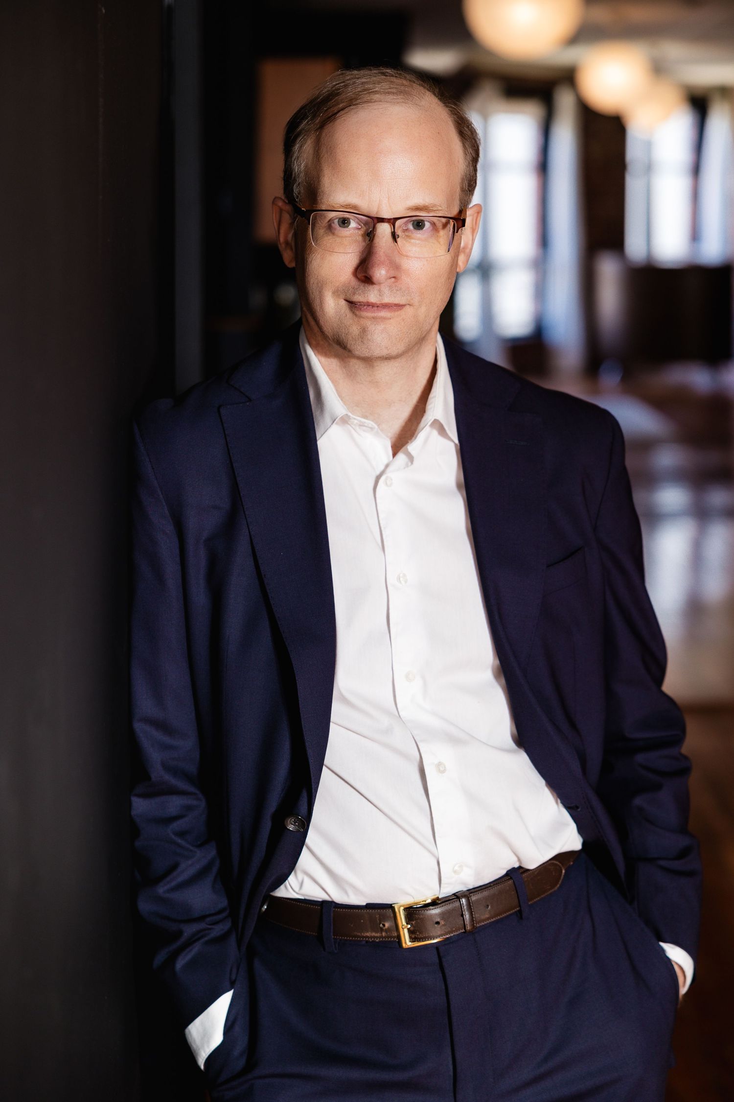 Business portraits of person in navy suit and white shirt against dark hallway.