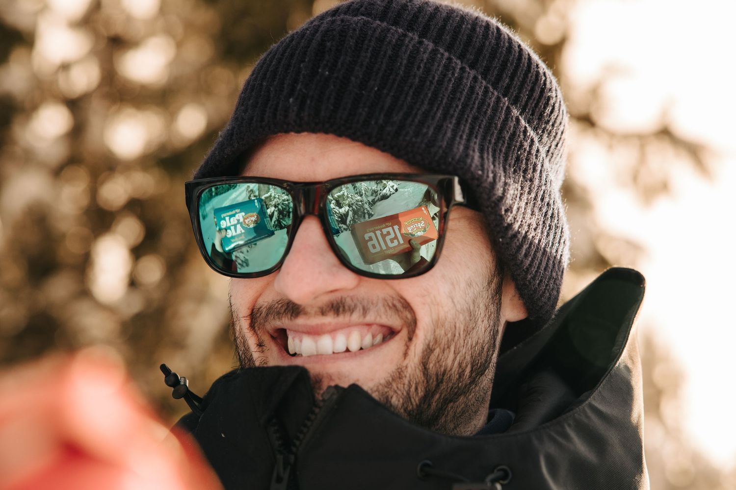 Close-up of person wearing winter hat and reflective sunglasses in snowy setting.