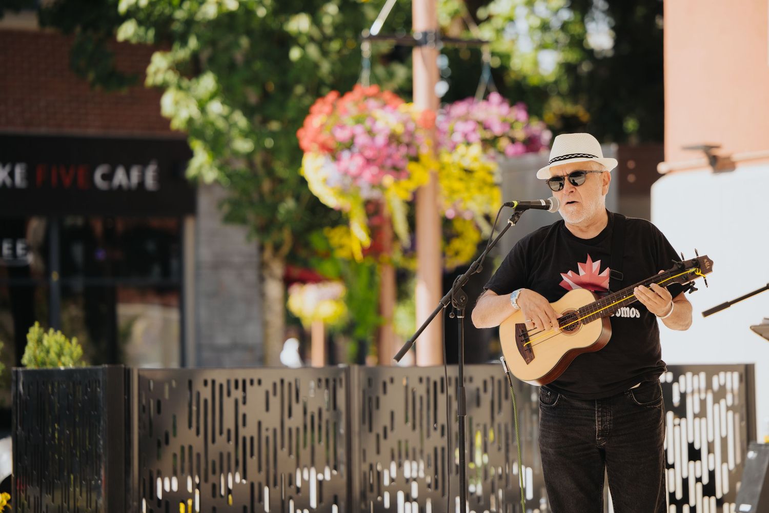 Musicians performing on an outdoor stage with cafe and street scenery in background.