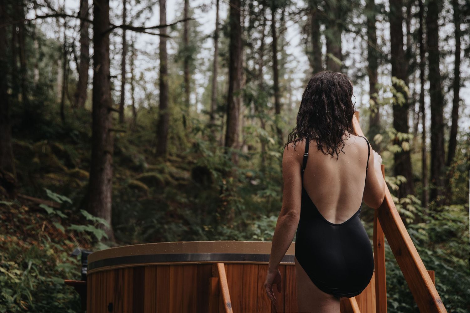 Wooden hot tub surrounded by tall pine trees in forest setting.