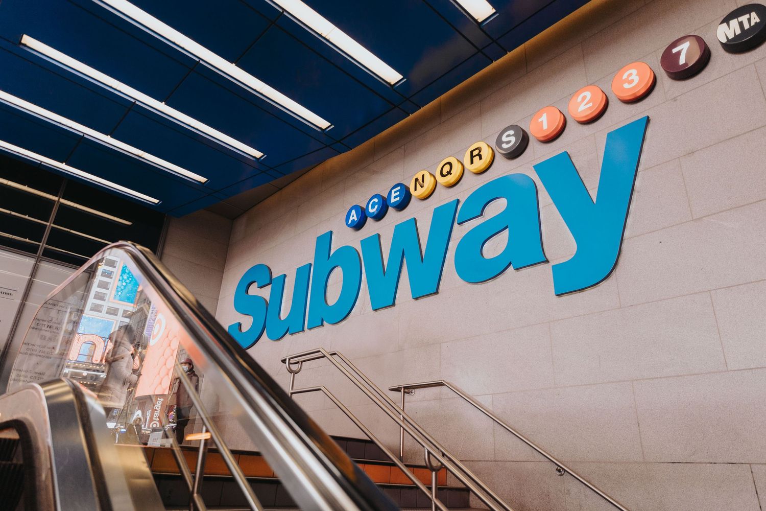 Modern subway station interior with illuminated signage and white ceiling.