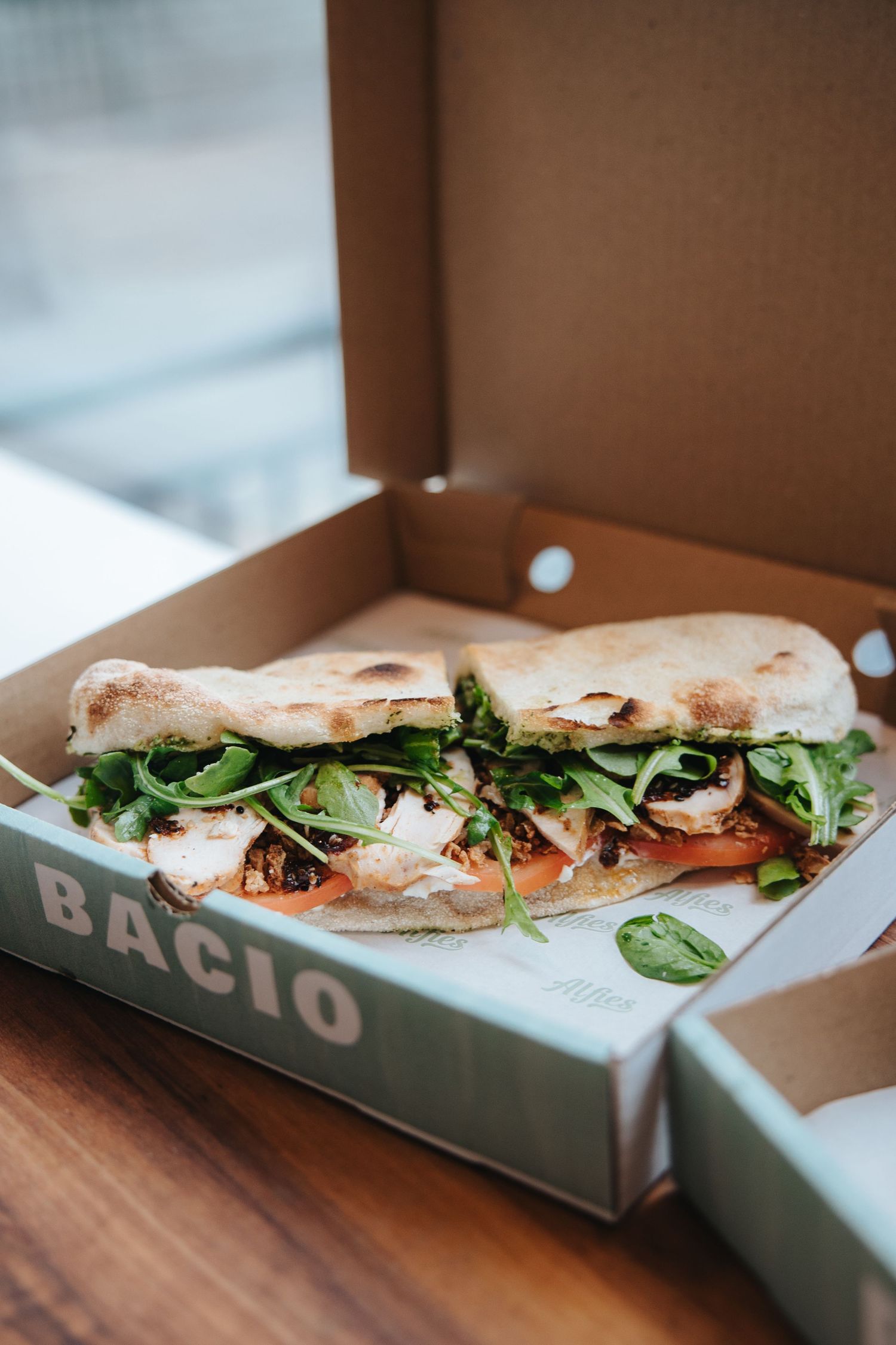 Fresh submarine sandwich filled with vegetables and greens in a takeout box.