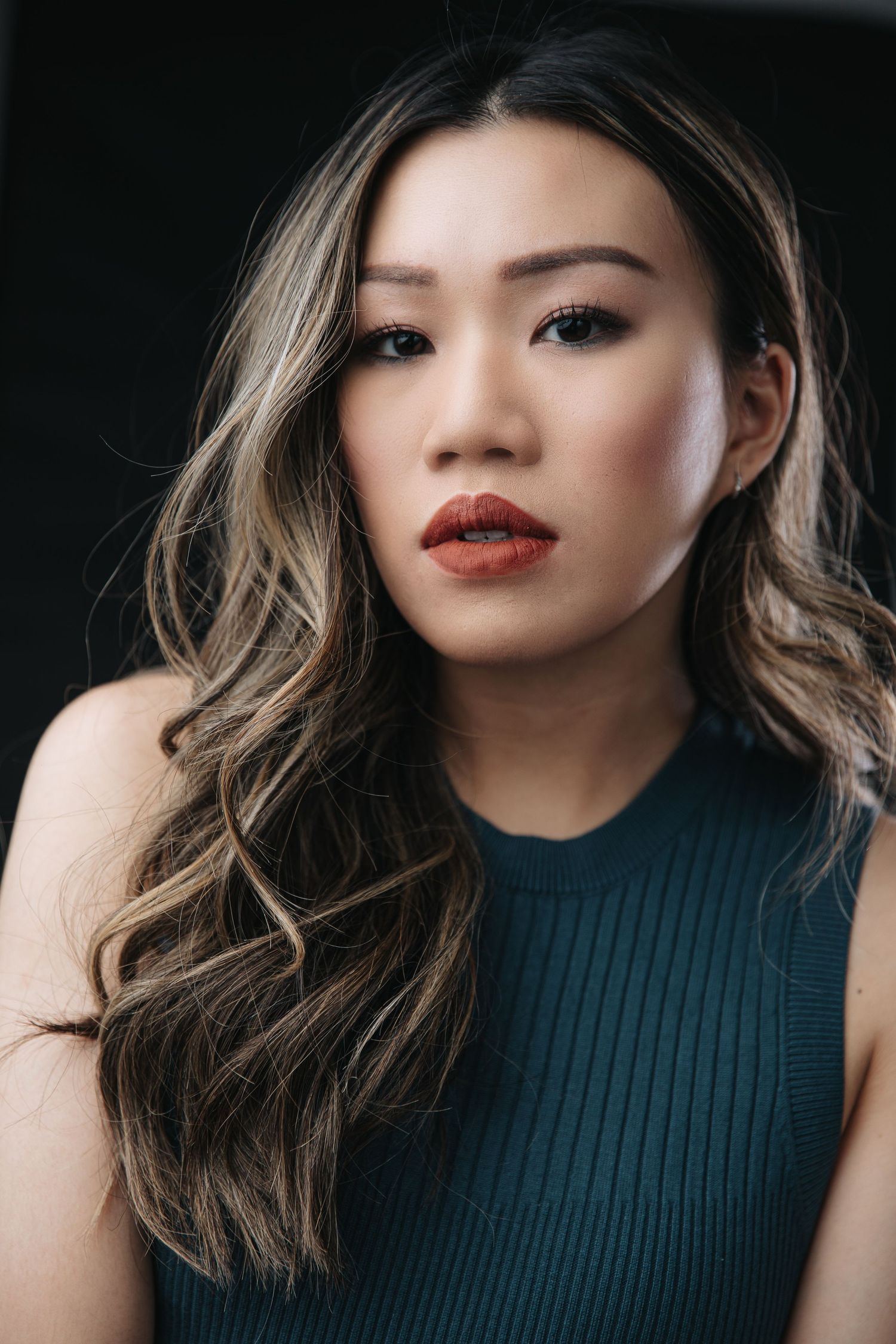 Close-up beauty shot of person with styled hair and red lipstick wearing dark top.