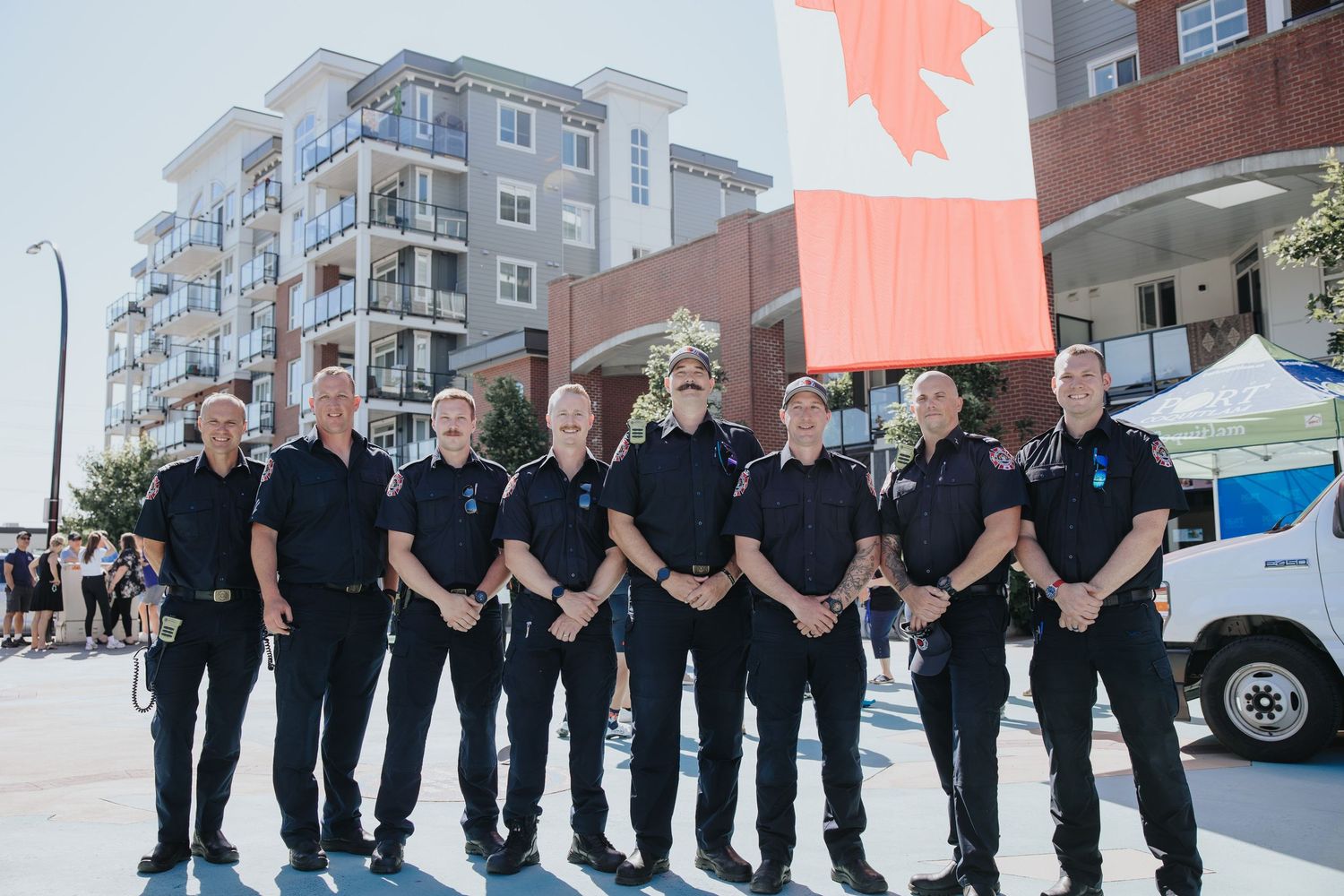 Line of uniformed personnel standing together under a large Canadian flag.