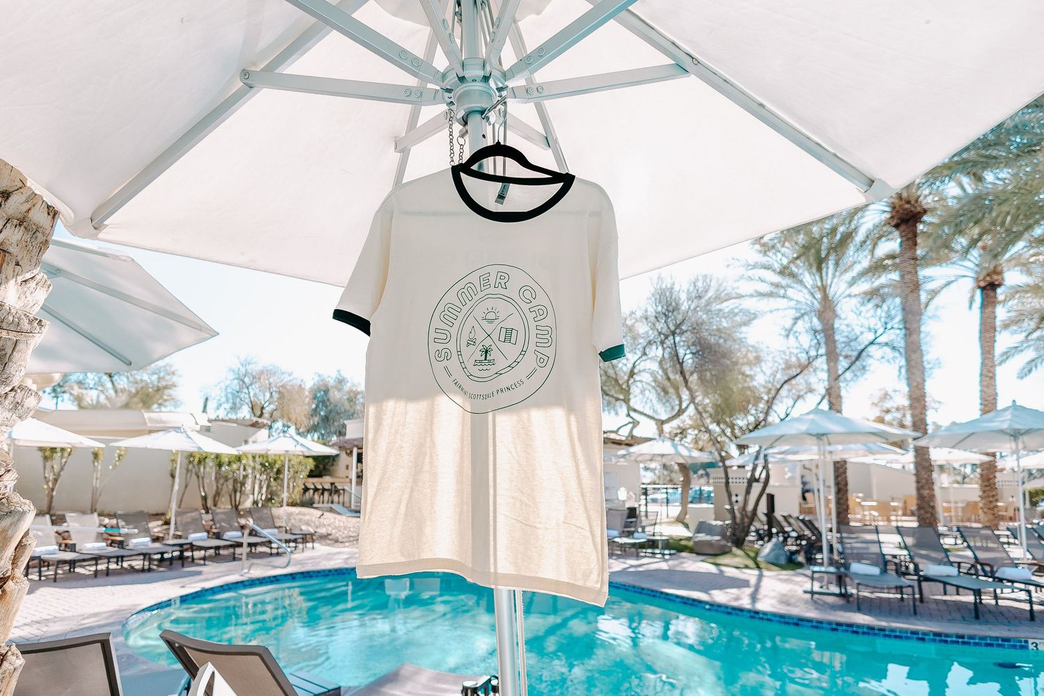 Resort pool area with white umbrellas and turquoise water under covered pavilion.